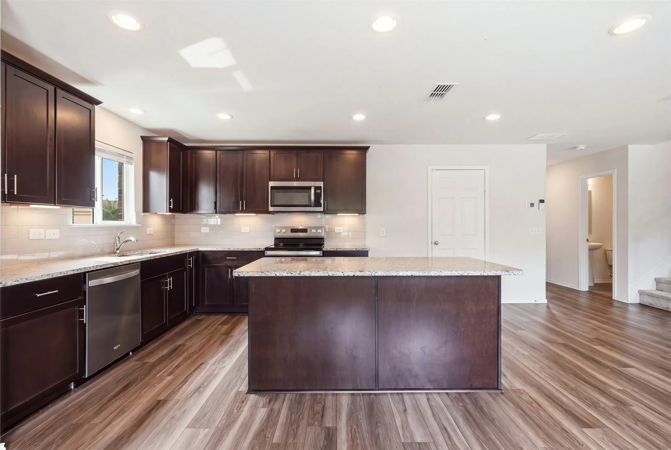 Stylish dark cabinetry, granite-style countertops, stainless steel appliances, wood-look floors, and recessed lighting