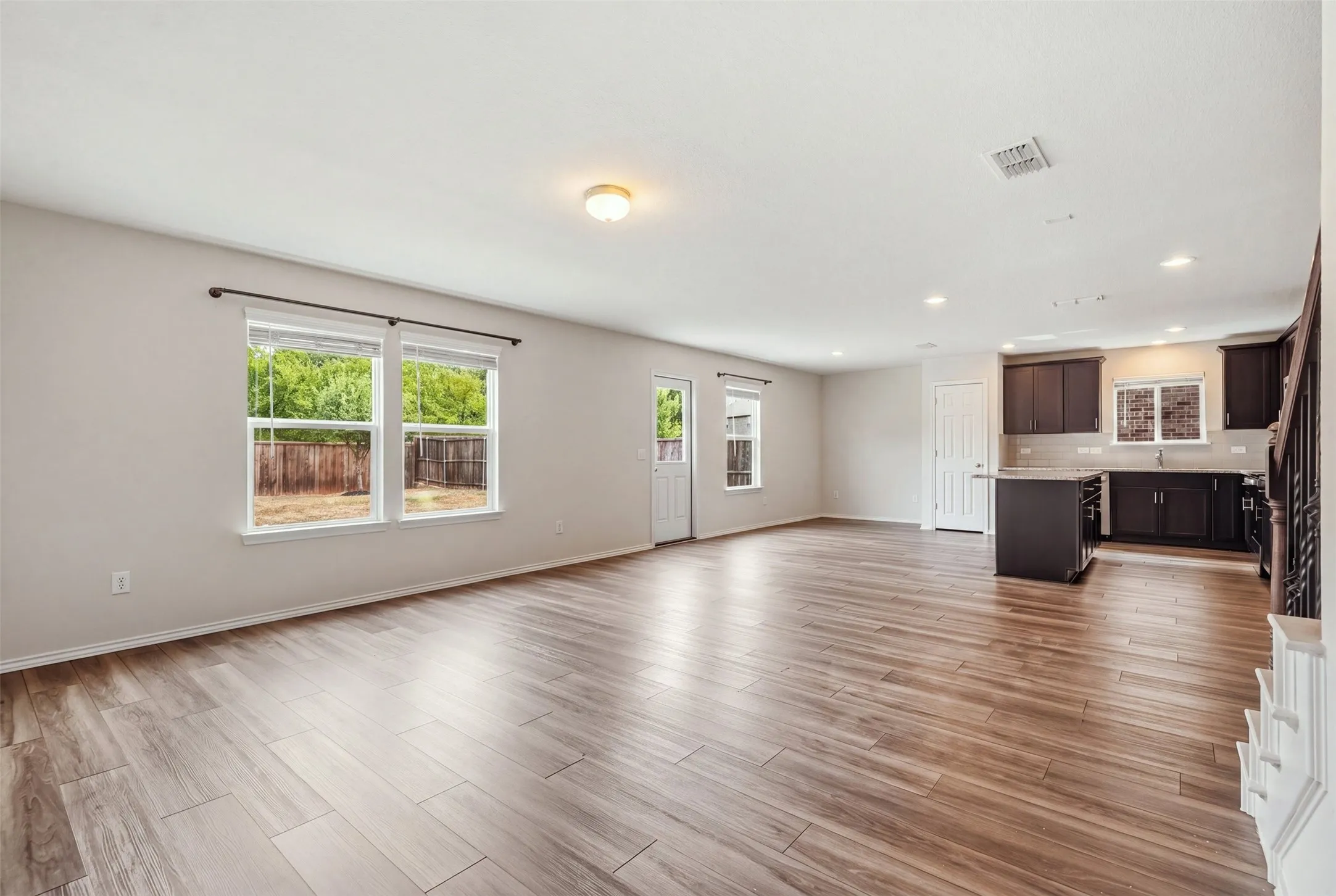 Spacious open-concept living with warm wood-look floors, recessed lighting, and a stylish island kitchen with dark cabinetry and stainless steel appliances