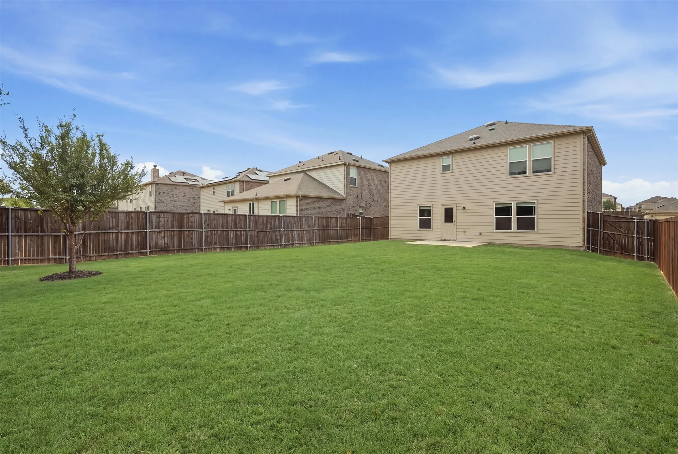 Spacious fenced backyard with a concrete patio, mature tree, and charming two-story exterior with brick accents