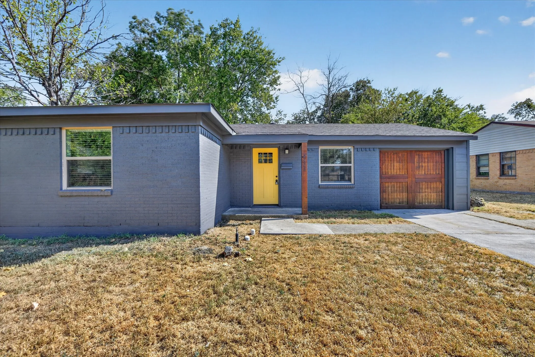 Single-story residence featuring a painted brick exterior, a vibrant yellow entry door, and a wood-paneled garage door