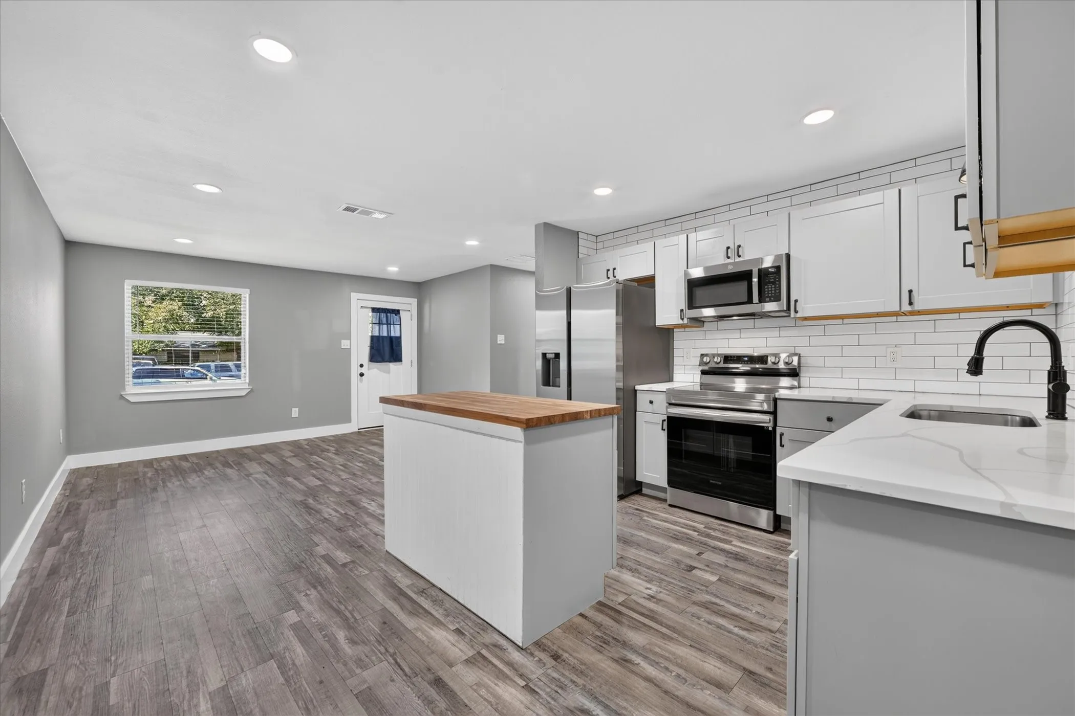 Open-concept living space featuring wood-finish flooring, recessed lighting, and a kitchen with stainless steel appliances, white subway tile backsplash, and light-toned cabinetry