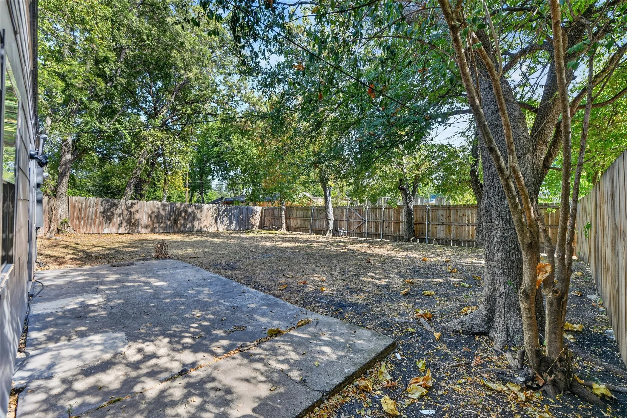 Spacious backyard featuring a concrete patio, wood privacy fence, and mature trees