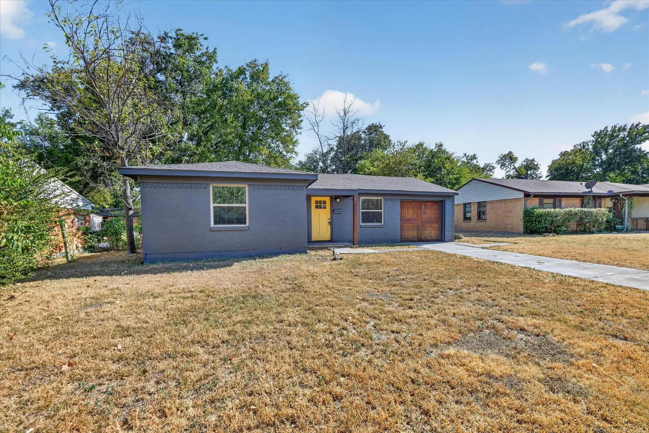 Single-story exterior with a gray painted finish, yellow entry door, and an attached garage with a wood-finish door