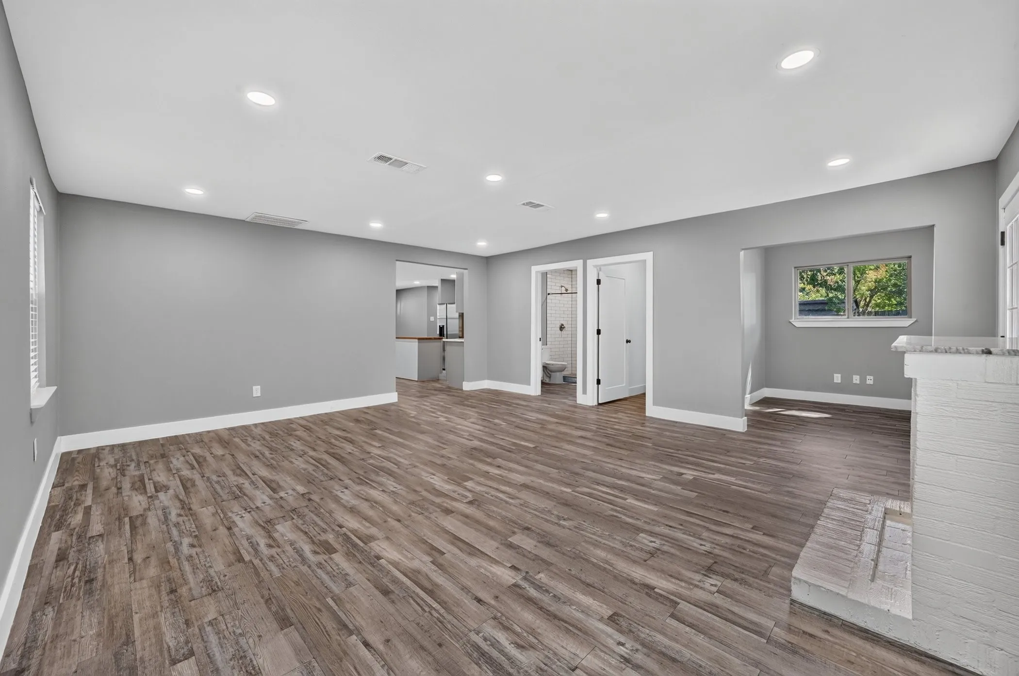Expansive room featuring wood-finish flooring, recessed lighting, a white painted brick fireplace with a stone hearth, and white trim throughout
