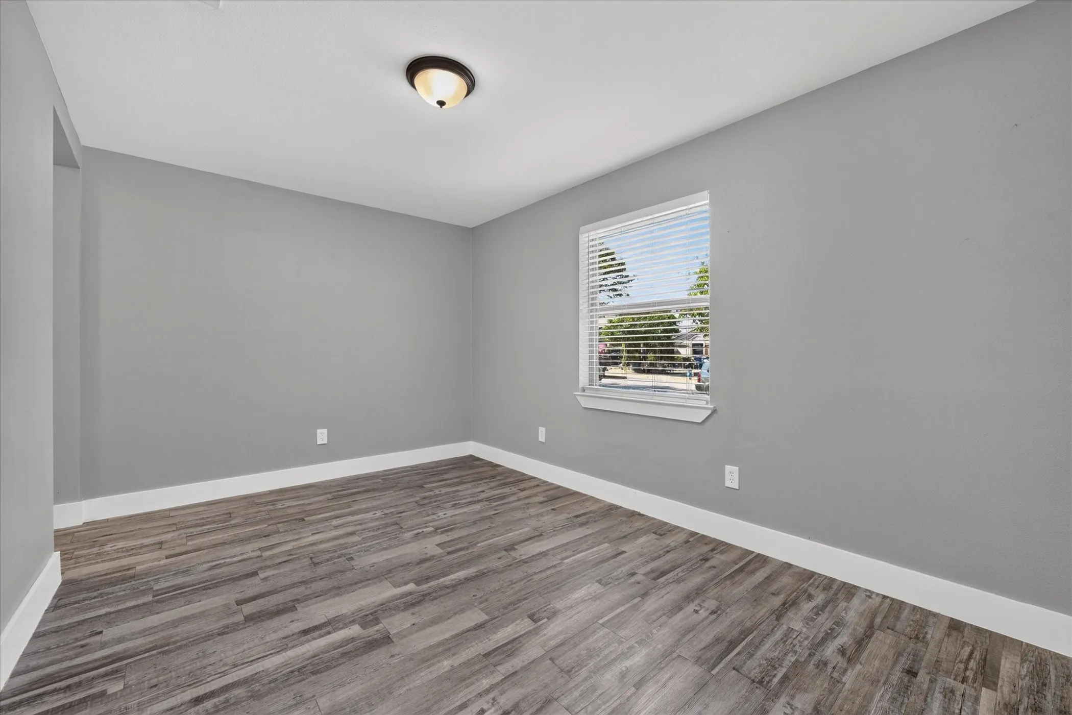 Neutral gray wall paint, wood-finish flooring, white window trim, white baseboards, and a semi-flush mount ceiling light