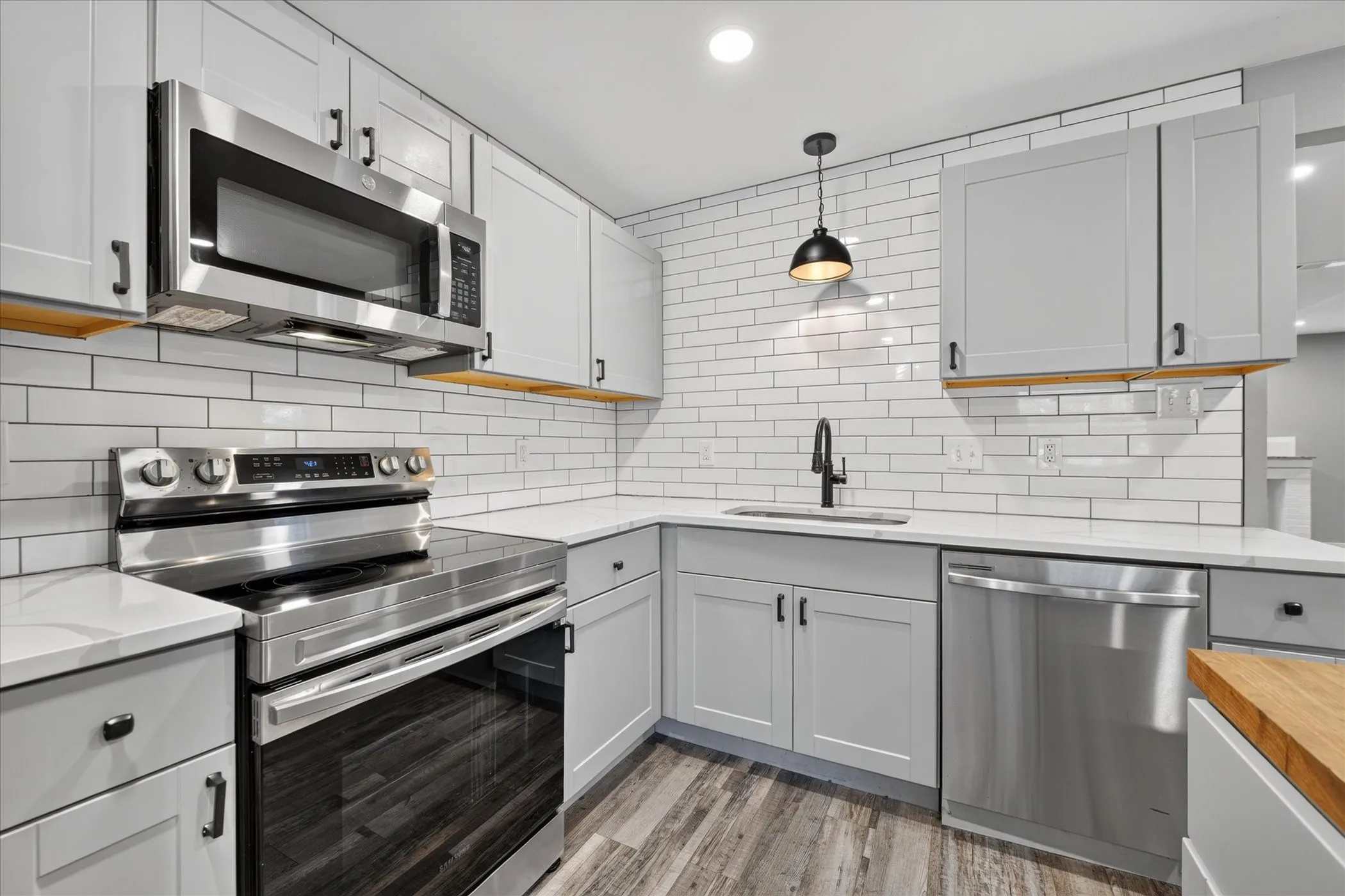 Modern kitchen featuring light gray cabinetry, stainless steel appliances, white subway tile backsplash, and wood-finish flooring