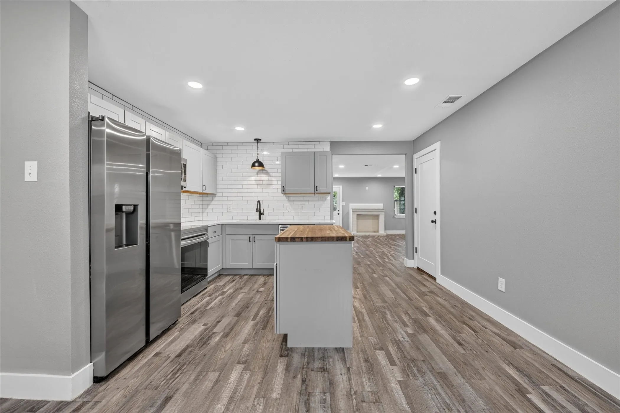 Kitchen featuring wood-finish flooring, stainless steel appliances, a center island with a wood countertop, and white subway tile backsplash