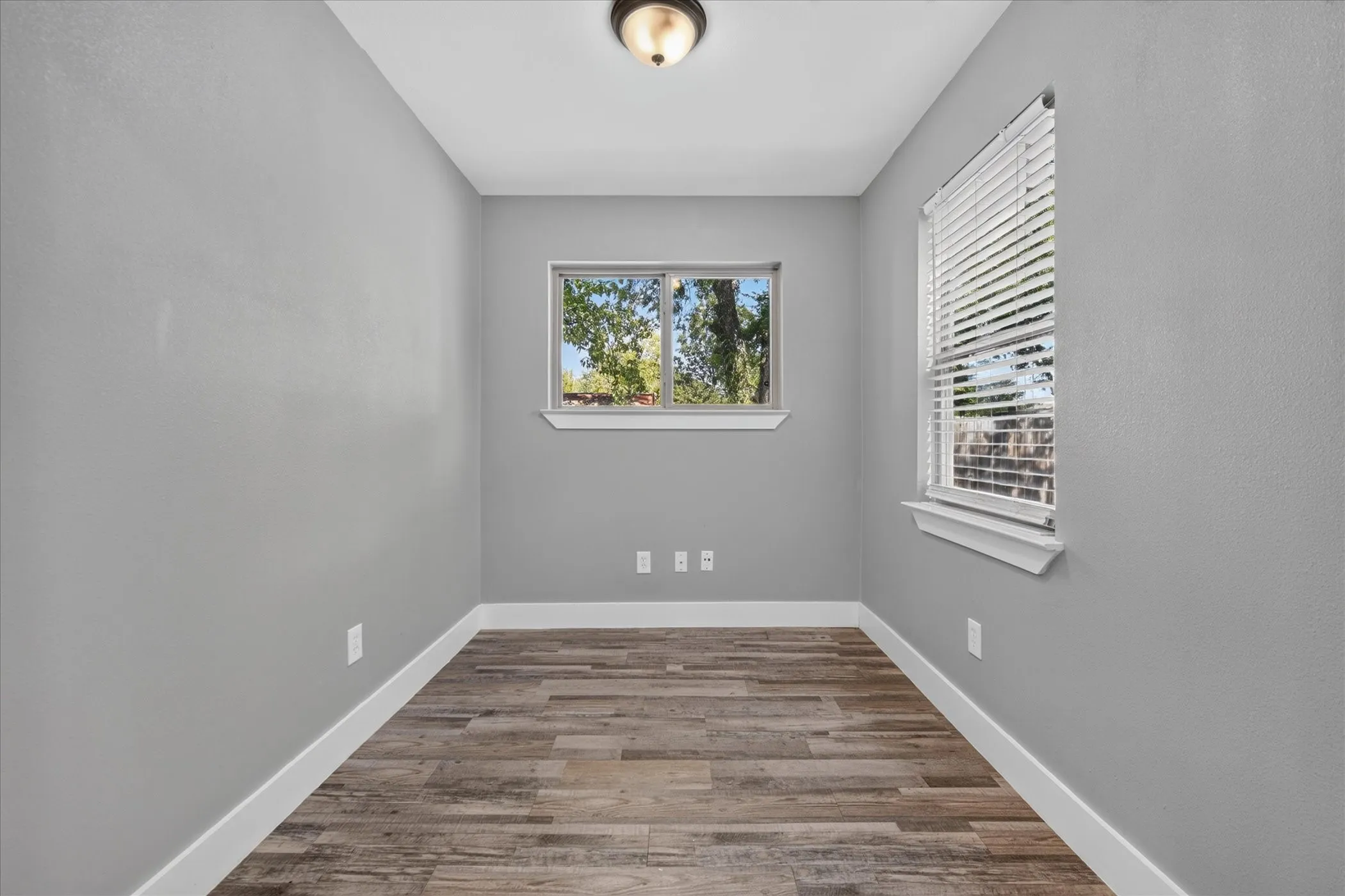 Wood-finish flooring, two windows with white blinds, and a flush mount ceiling light