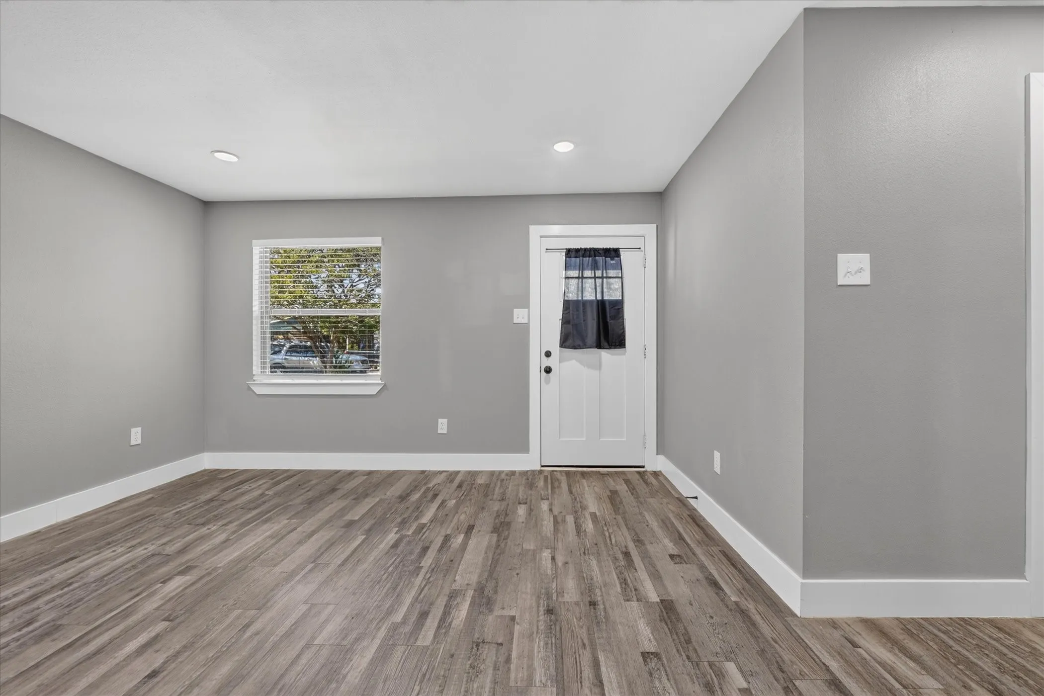Wood-finish flooring, recessed ceiling lighting, light gray wall paint, and white trim accents