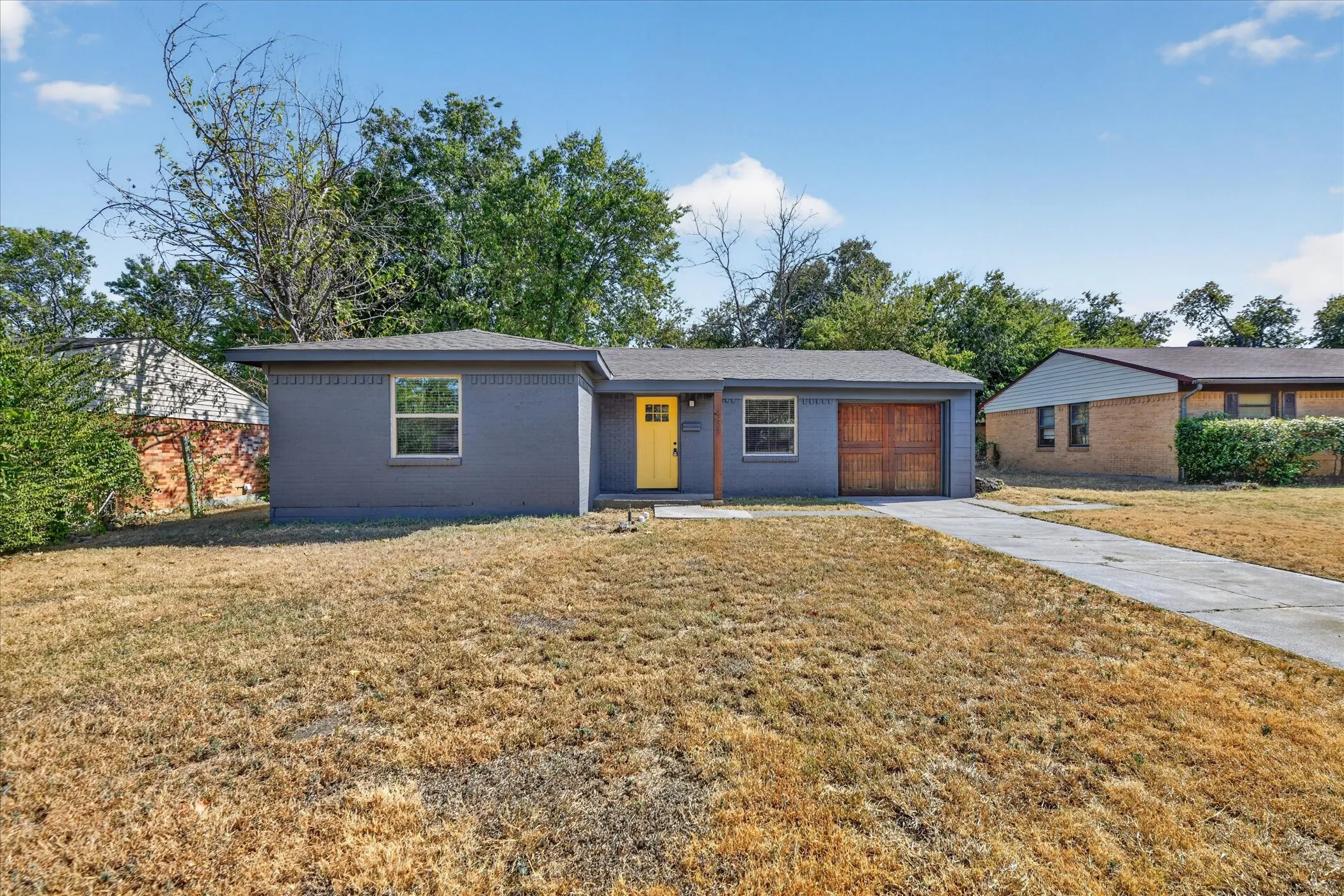 Single-story residence featuring a gray exterior, a vibrant yellow front door, and a wood-finish garage door