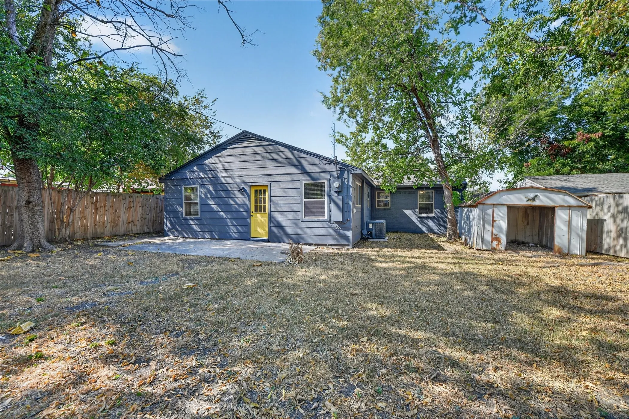 Rear exterior featuring gray siding, a yellow paneled door, a concrete patio, and a detached storage shed