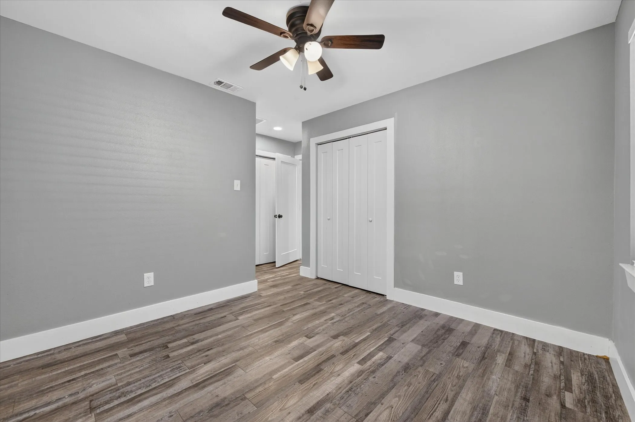 Wood-finish flooring, ceiling fan, bi-fold closet doors, white trim, and light gray walls