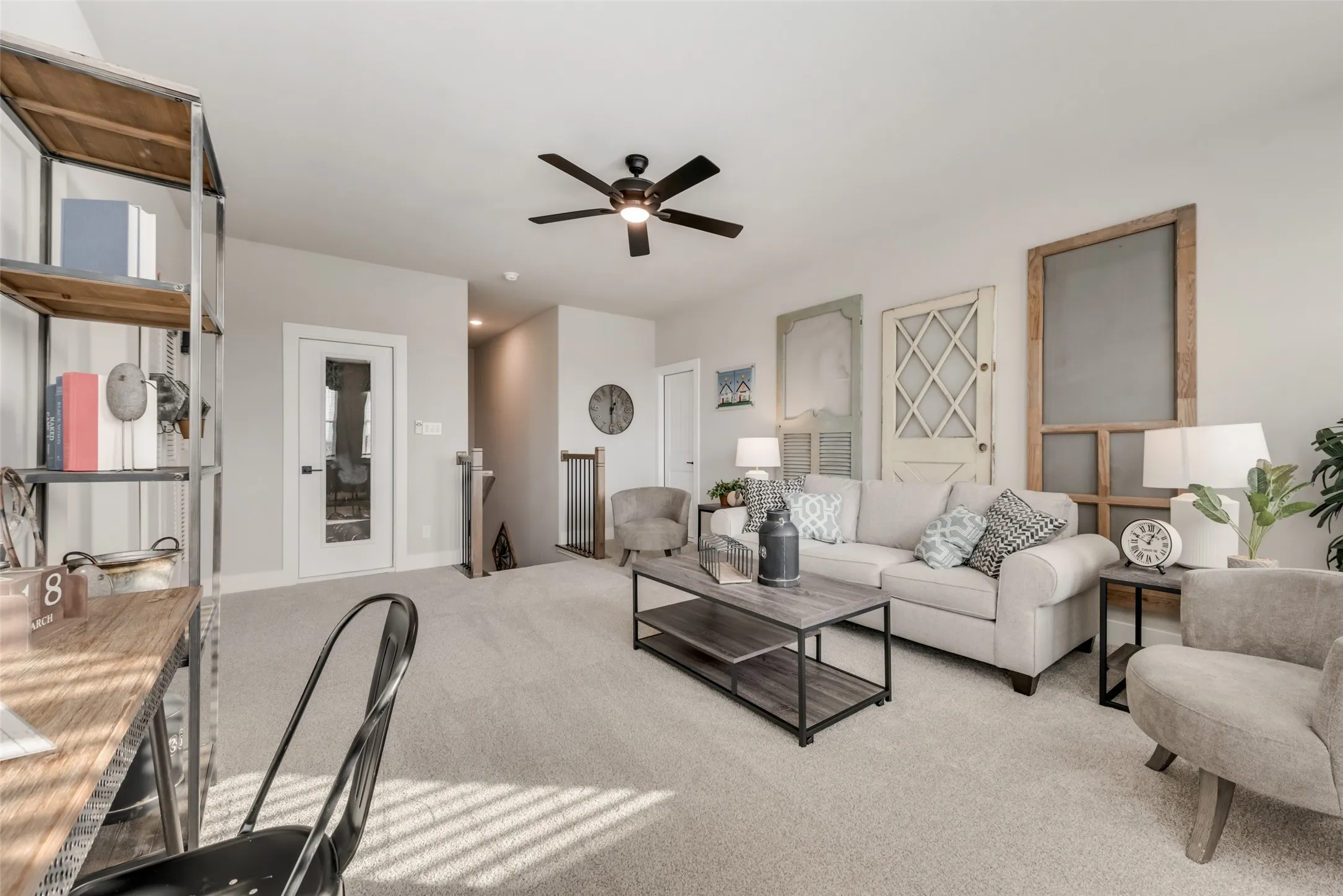 Carpeted living area featuring a ceiling fan, a glass-paned interior door, and an open staircase