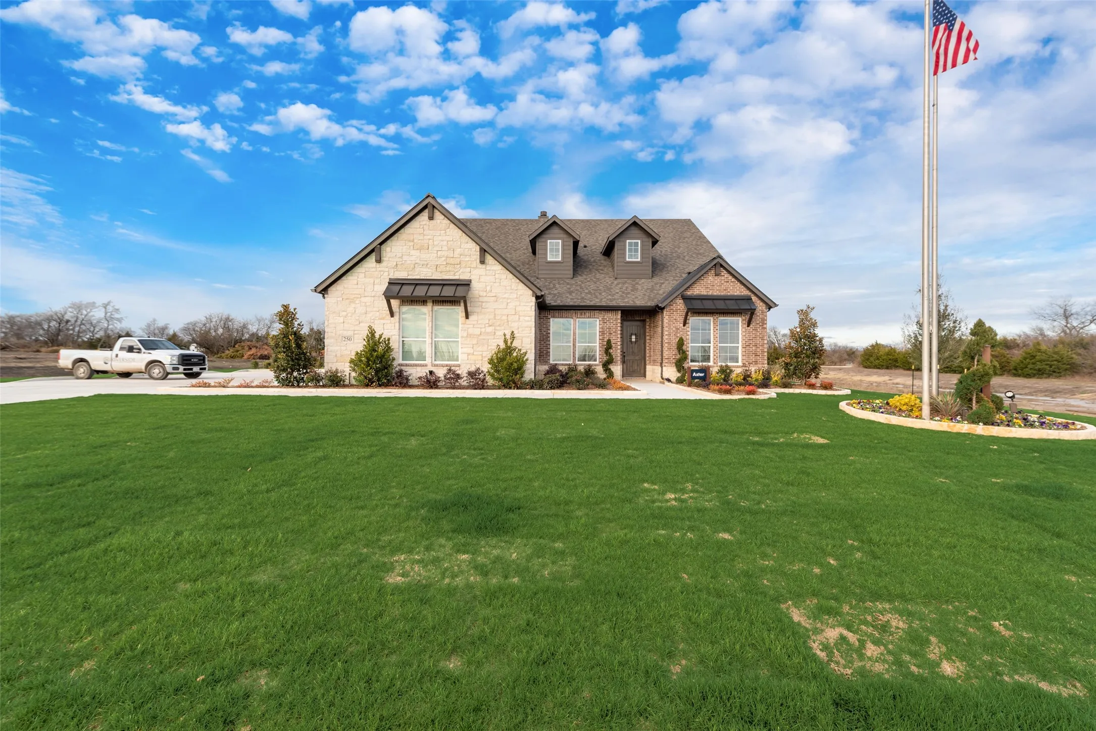 Brick and stone exterior featuring dormer windows, a concrete driveway, and a manicured lawn with a landscaped planting bed