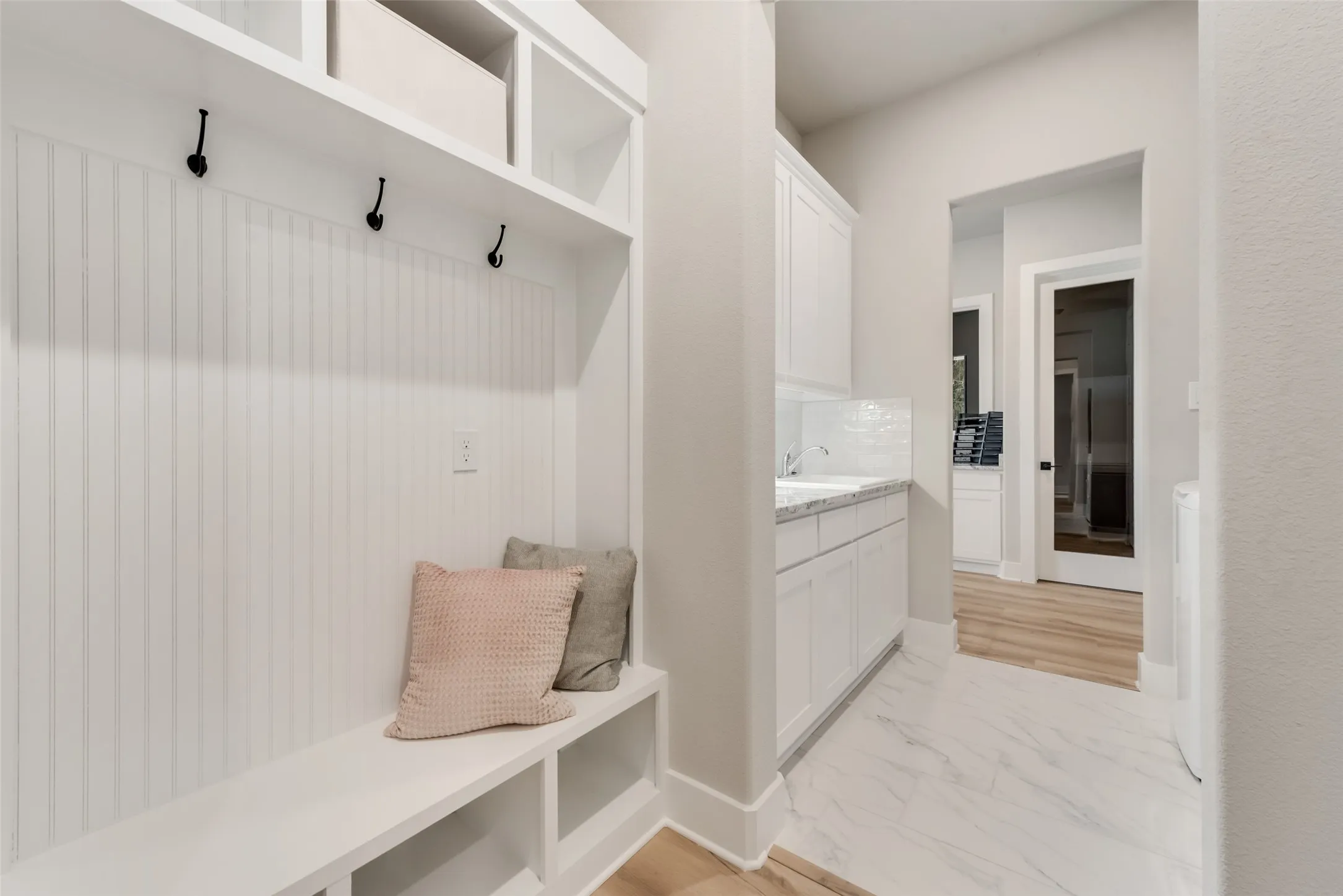 Built-in mudroom bench with storage, white beadboard paneling, and wall hooks