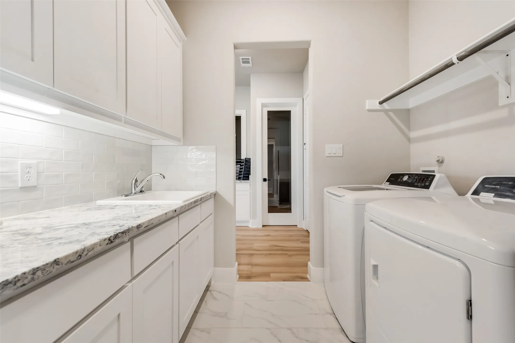 Laundry area featuring white cabinetry, a built-in sink, granite-style countertop, subway tile backsplash, and overhead shelving