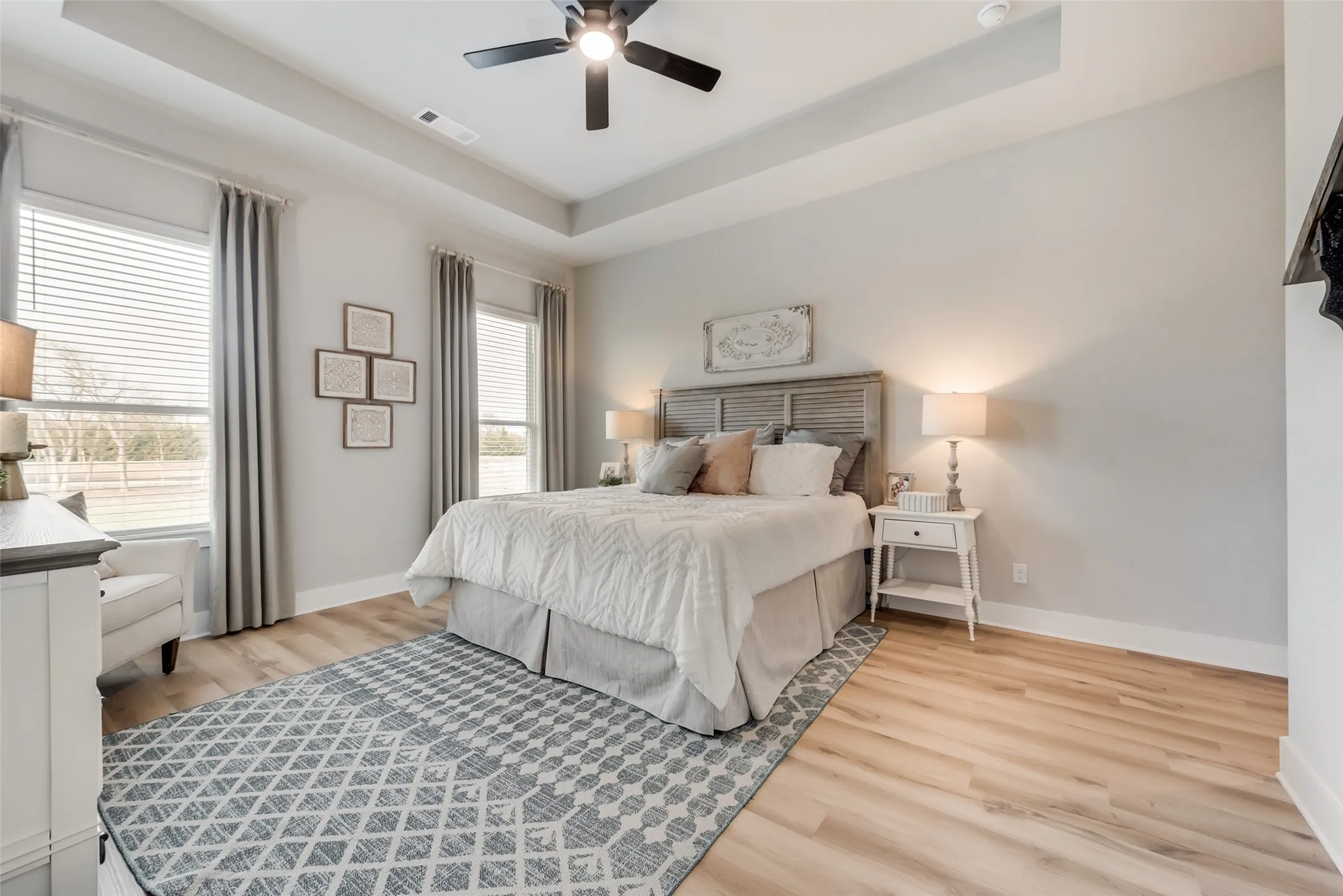 Tray ceiling with a black ceiling fan, wood-finish flooring, and multiple windows