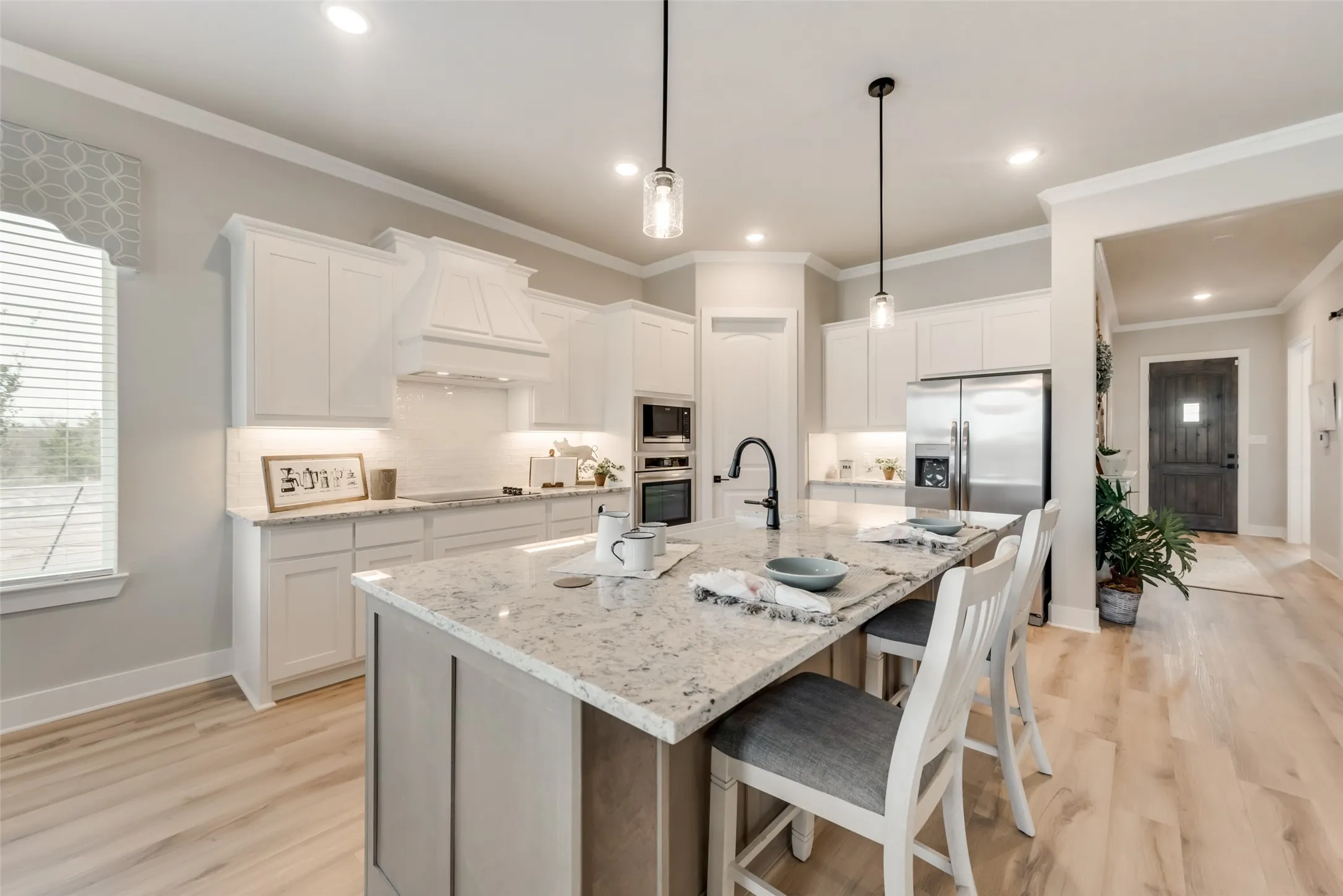 Kitchen featuring a large central island with seating, white cabinetry, integrated stainless steel appliances, wood-finish flooring, and pendant lighting
