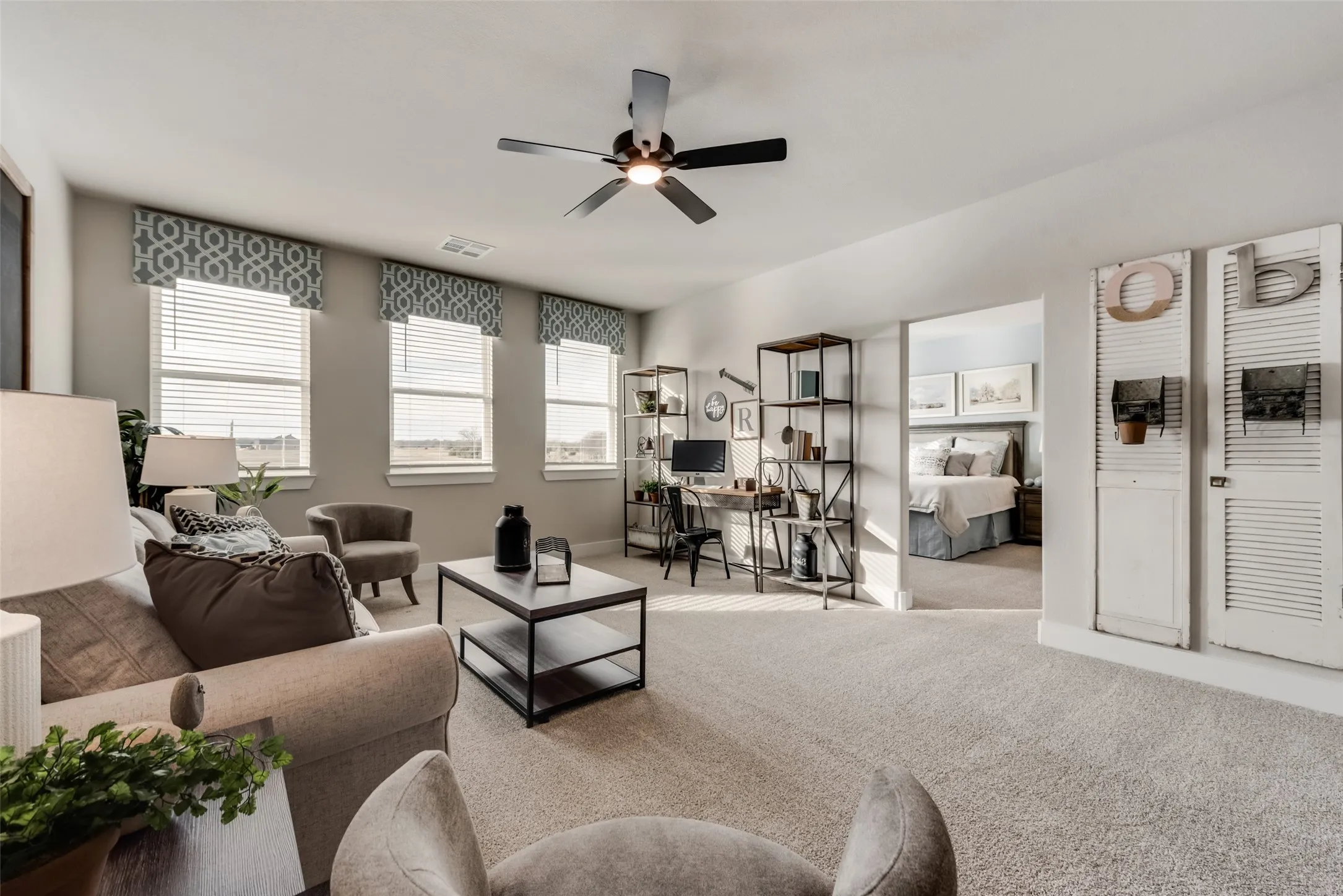 Spacious carpeted living area with multiple windows, a ceiling fan, and an open doorway to another room