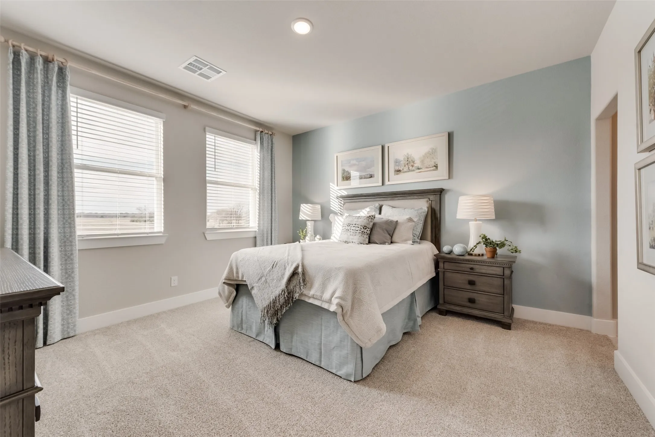 Light-colored carpeting, multiple windows with blinds, recessed ceiling lighting, light blue accent wall, and a wood-finish bed frame