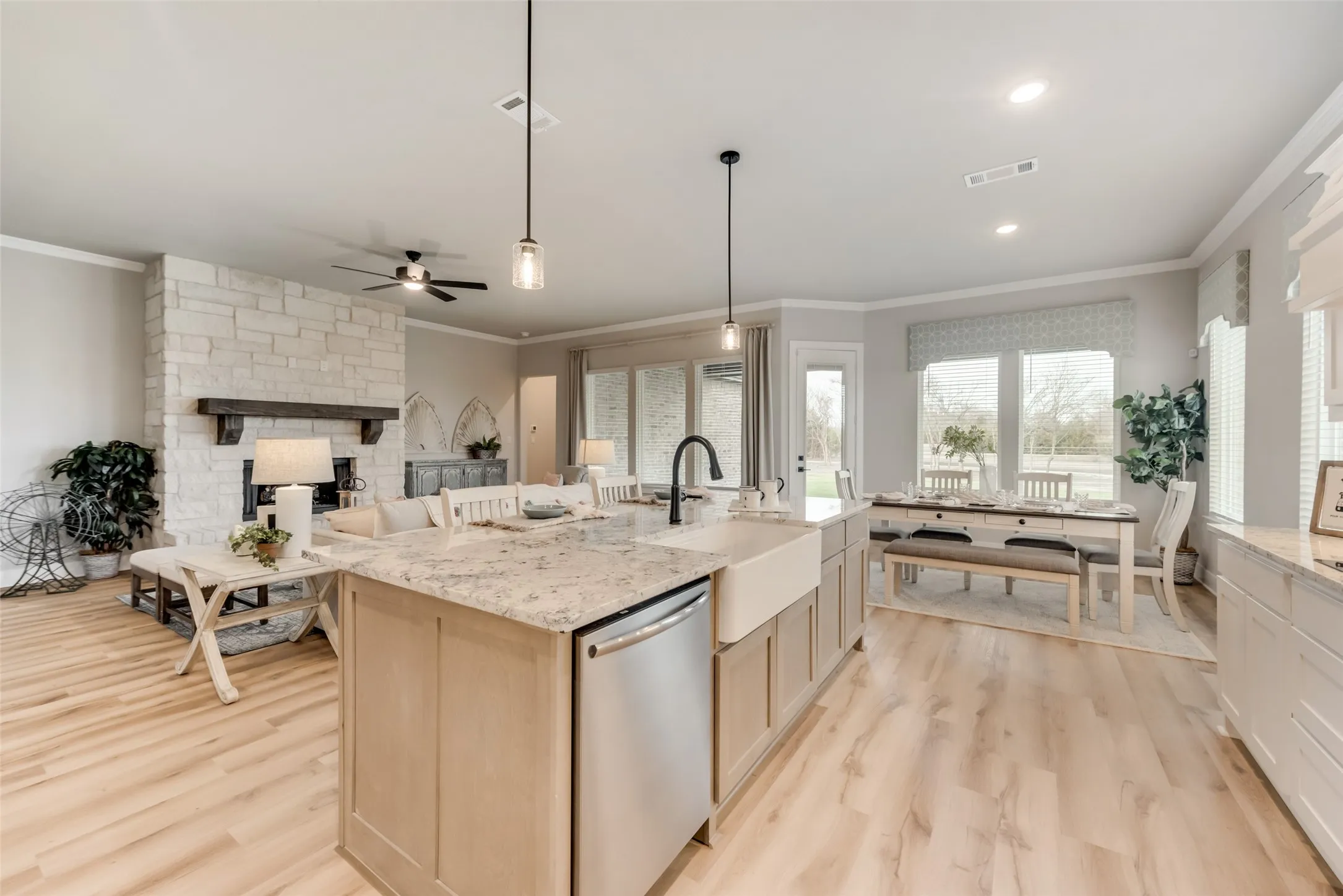 Open-concept kitchen and living area featuring wood-finish flooring, a stone fireplace, a kitchen island with granite countertop, and a farmhouse sink