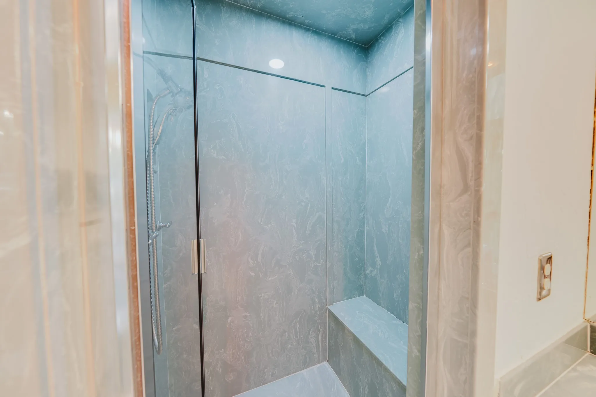 Enclosed shower featuring a built-in bench, recessed lighting, and a handheld shower fixture