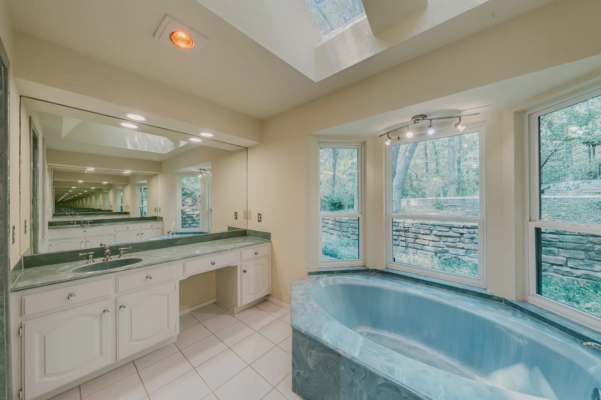 Recessed bathtub with a stone surround, large vanity with double sinks, skylight, and expansive windows