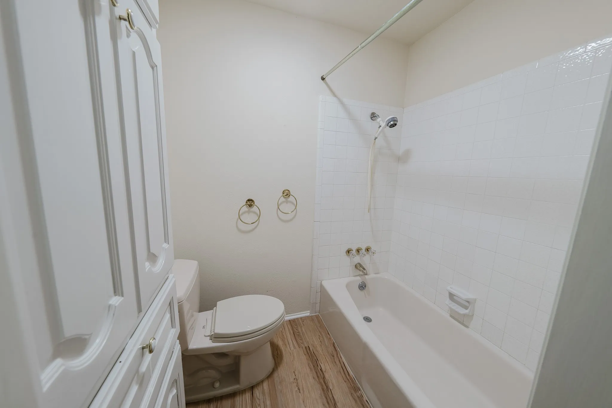 Built-in cabinetry, ceramic tile shower surround, bathtub with shower fixture, wood-finish flooring, and toilet
