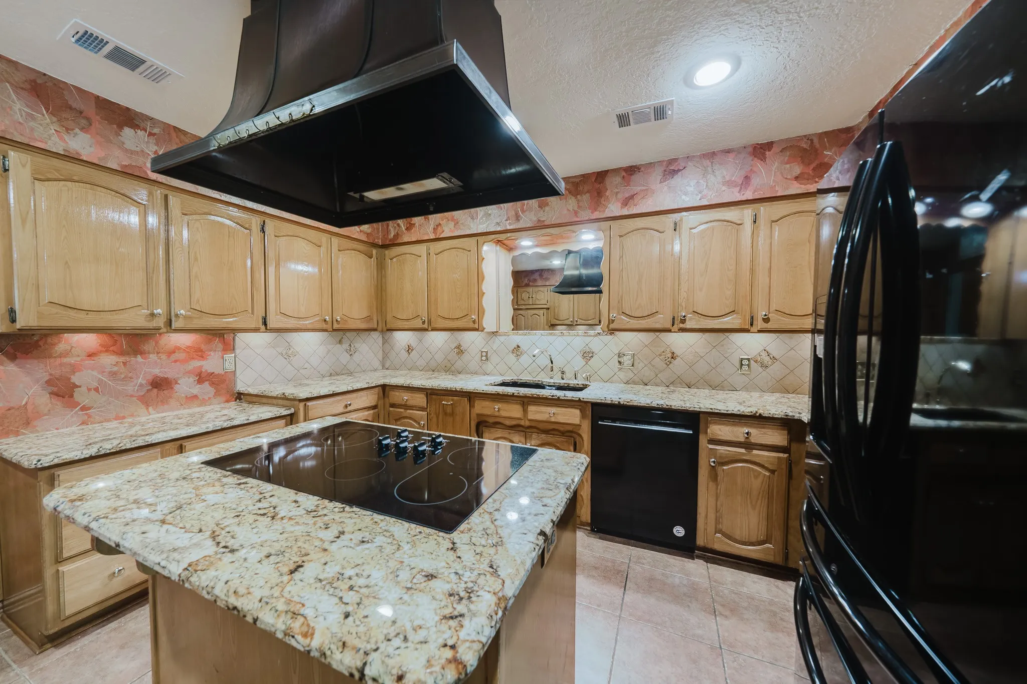 Kitchen featuring a central island with integrated cooktop, light wood cabinetry, stone countertops, and a tile backsplash
