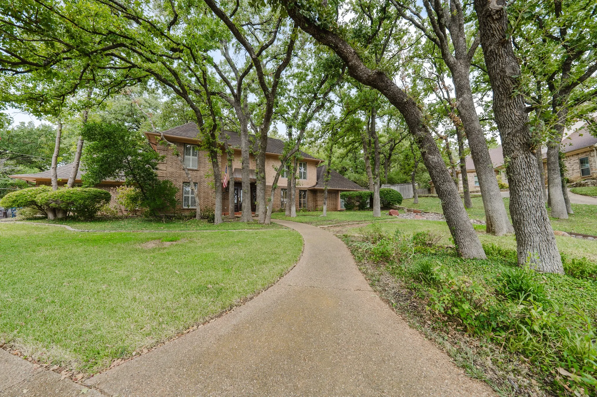 Brick-clad two-story residence featuring a paved walkway, mature trees, and a landscaped front yard