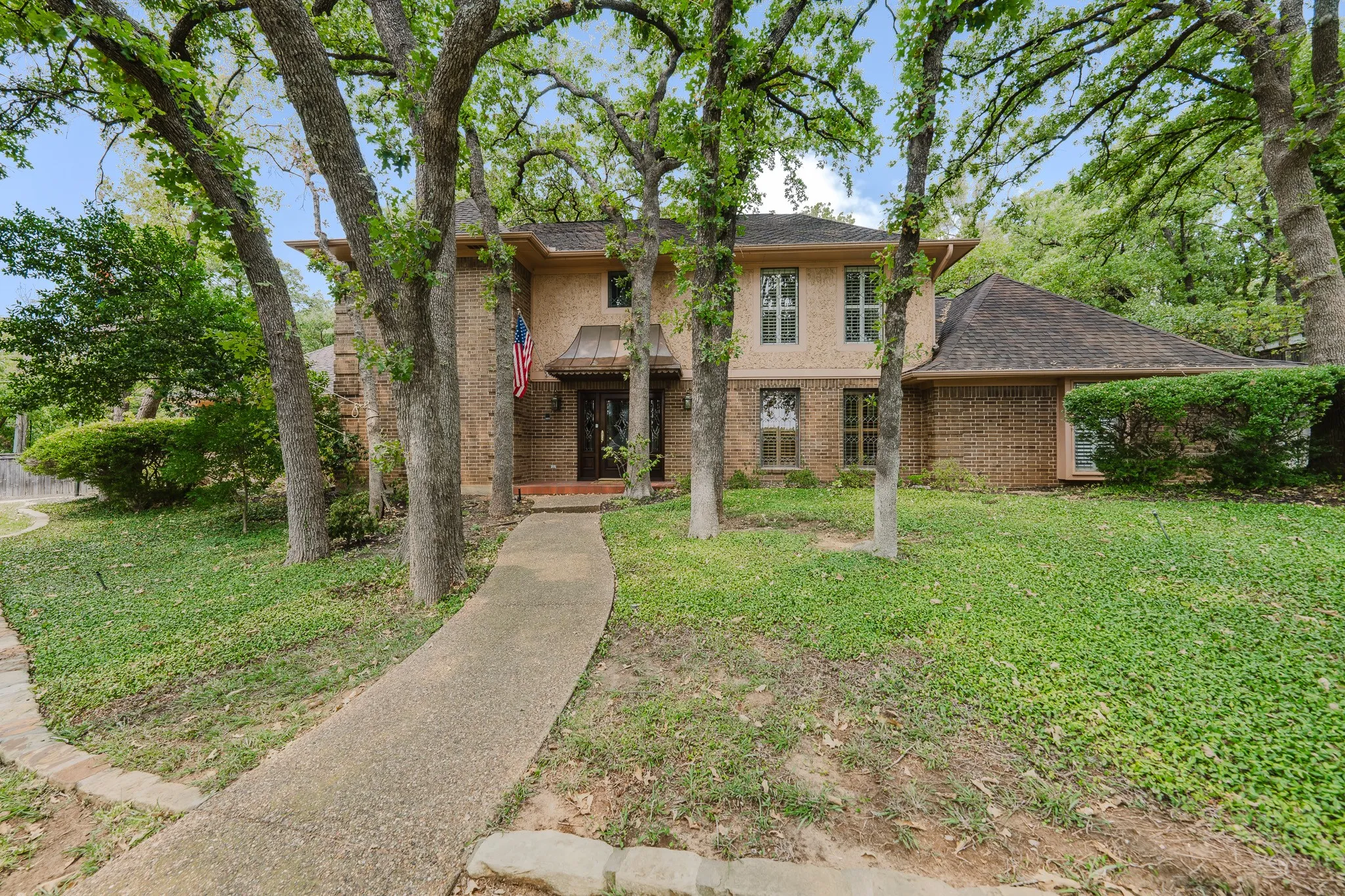 Brick exterior with stone accents, mature trees, and a concrete pathway