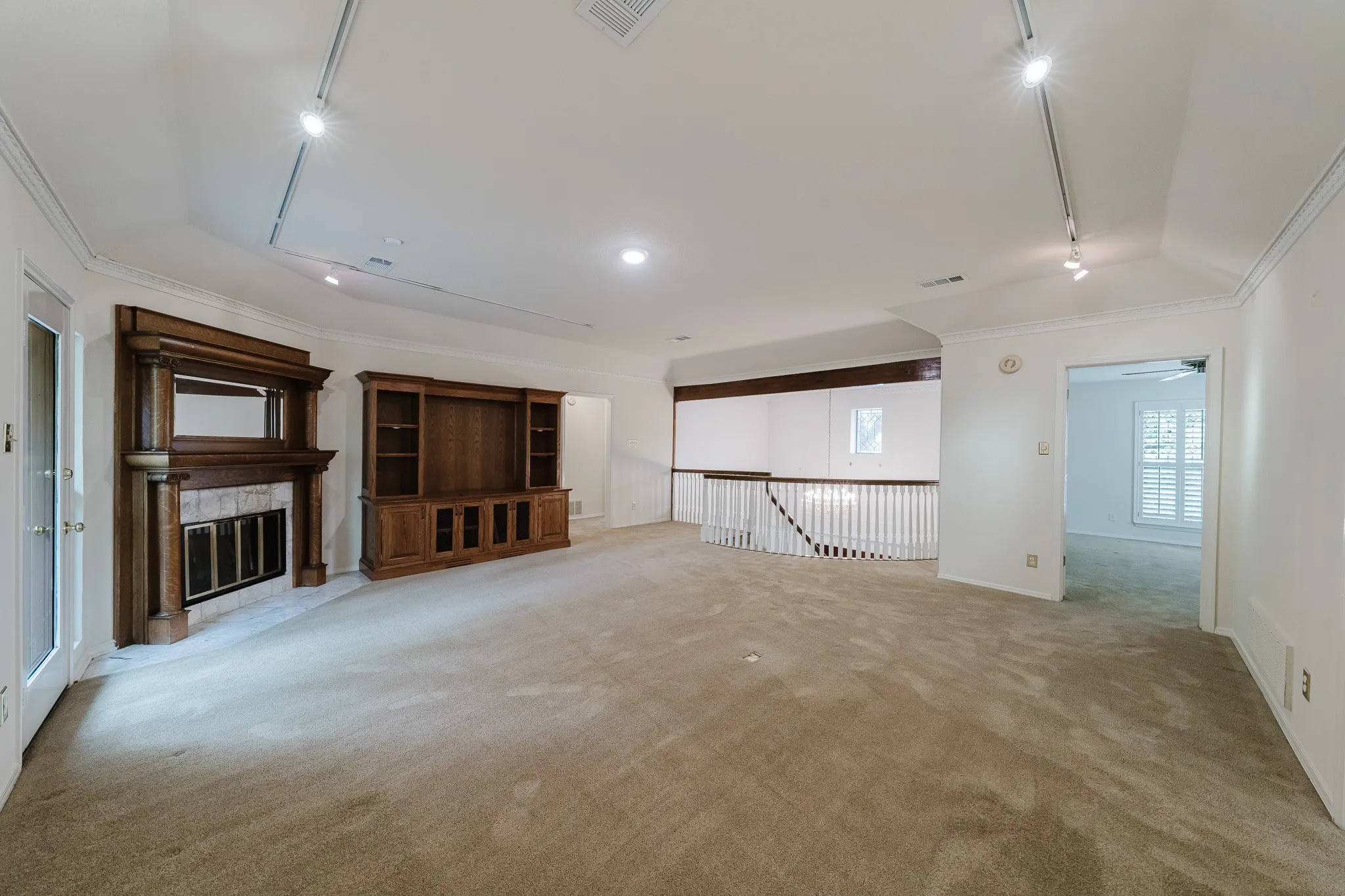 Spacious interior featuring a built-in media center, wood-mantled fireplace, and a white balustrade overlooking a lower level