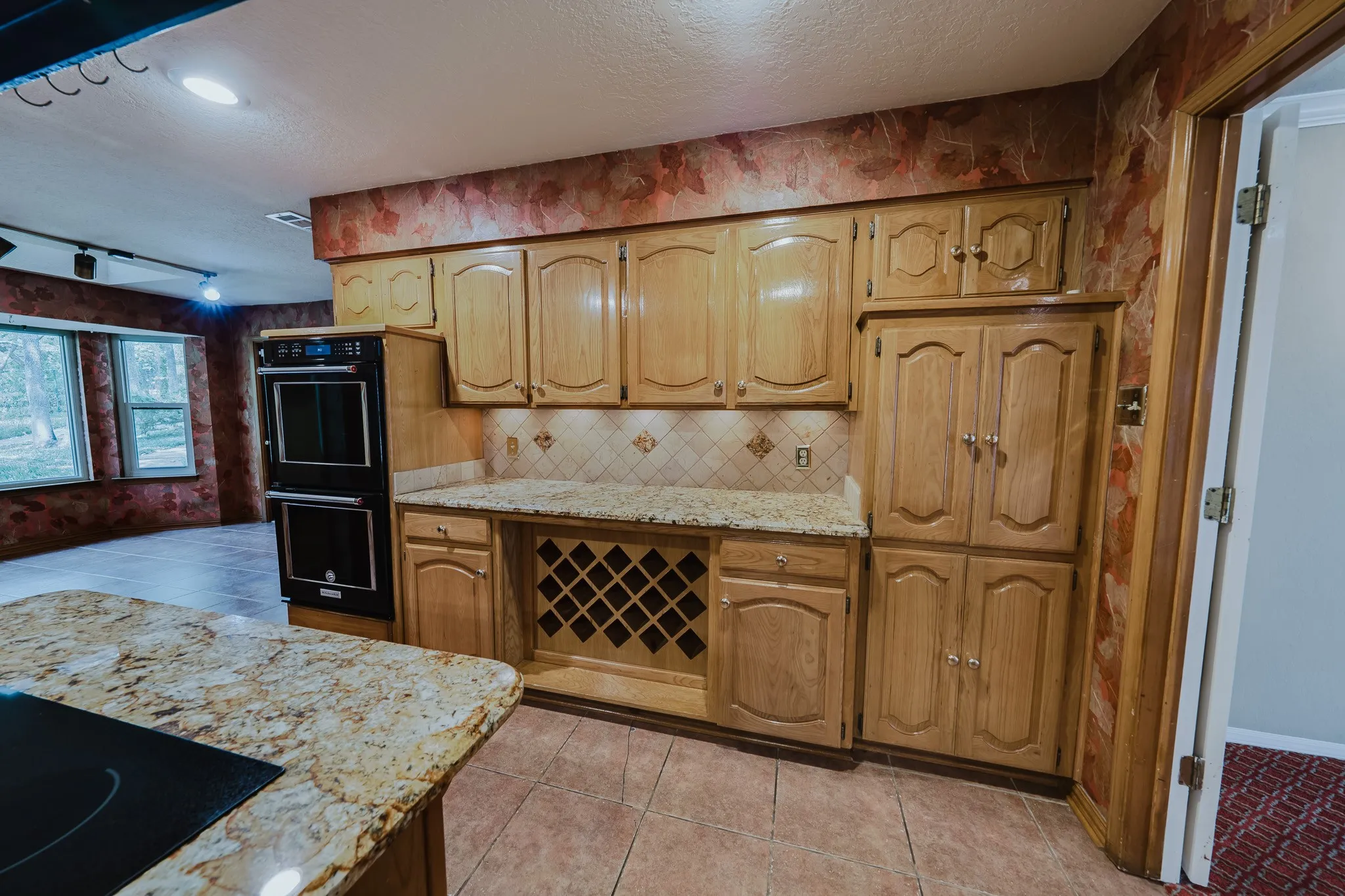 Kitchen featuring wood cabinetry, granite-style countertops, integrated double ovens, a built-in wine rack, and tile flooring