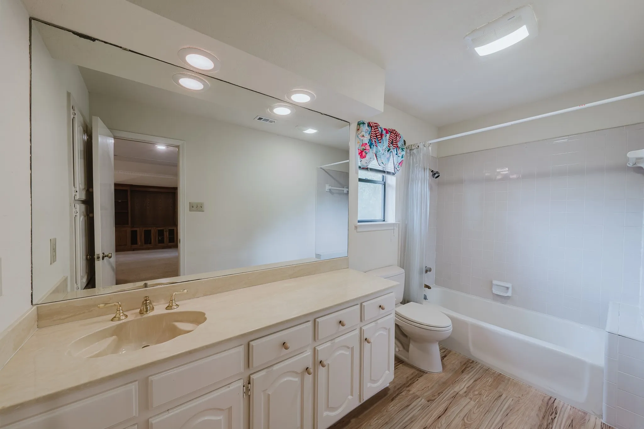 White vanity with integrated sink, gold-tone fixtures, and a large mirror with recessed lighting