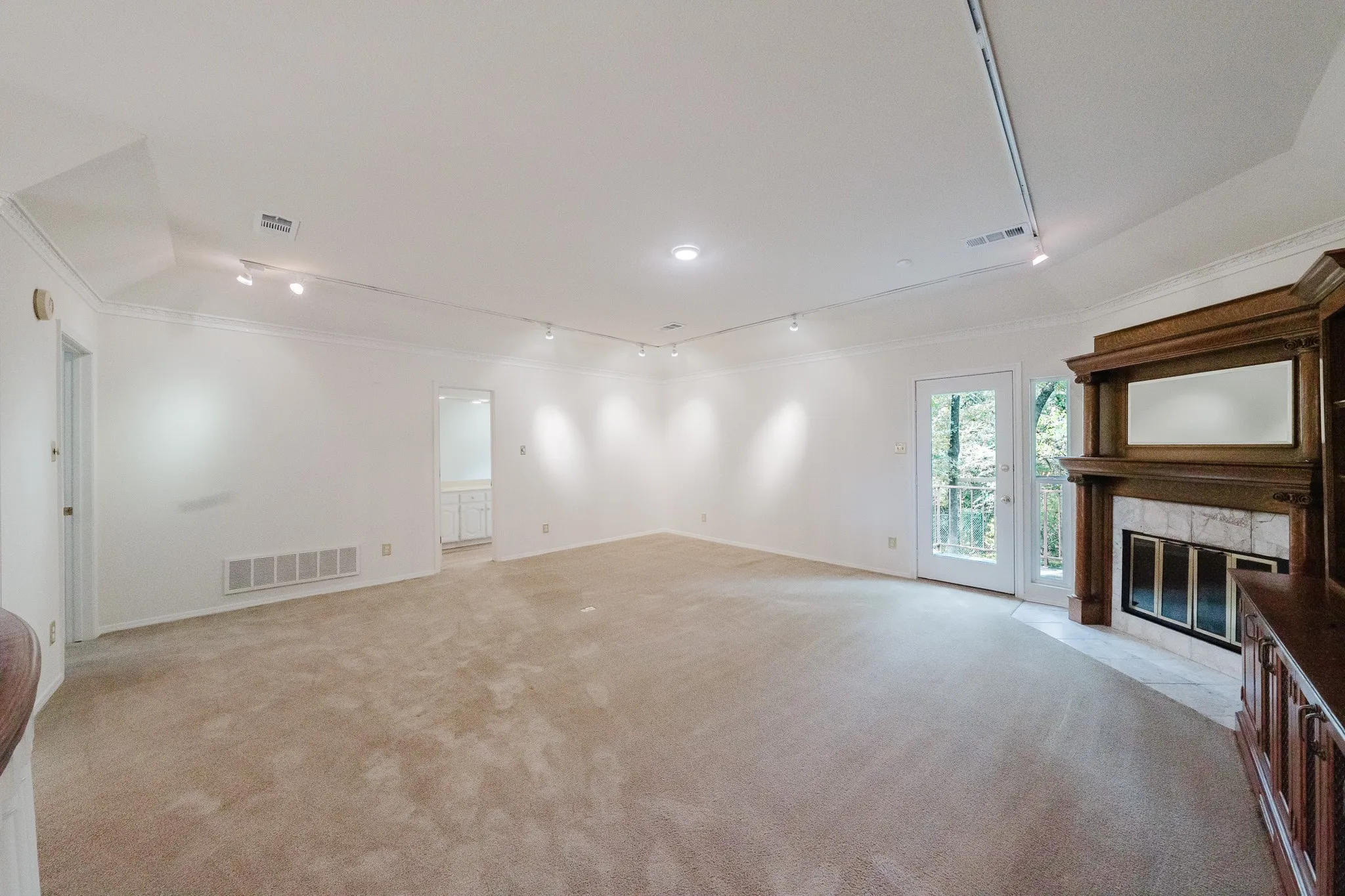 Spacious room featuring neutral carpeting, track lighting, crown molding, and a fireplace with a wood-finish mantel and tile surround