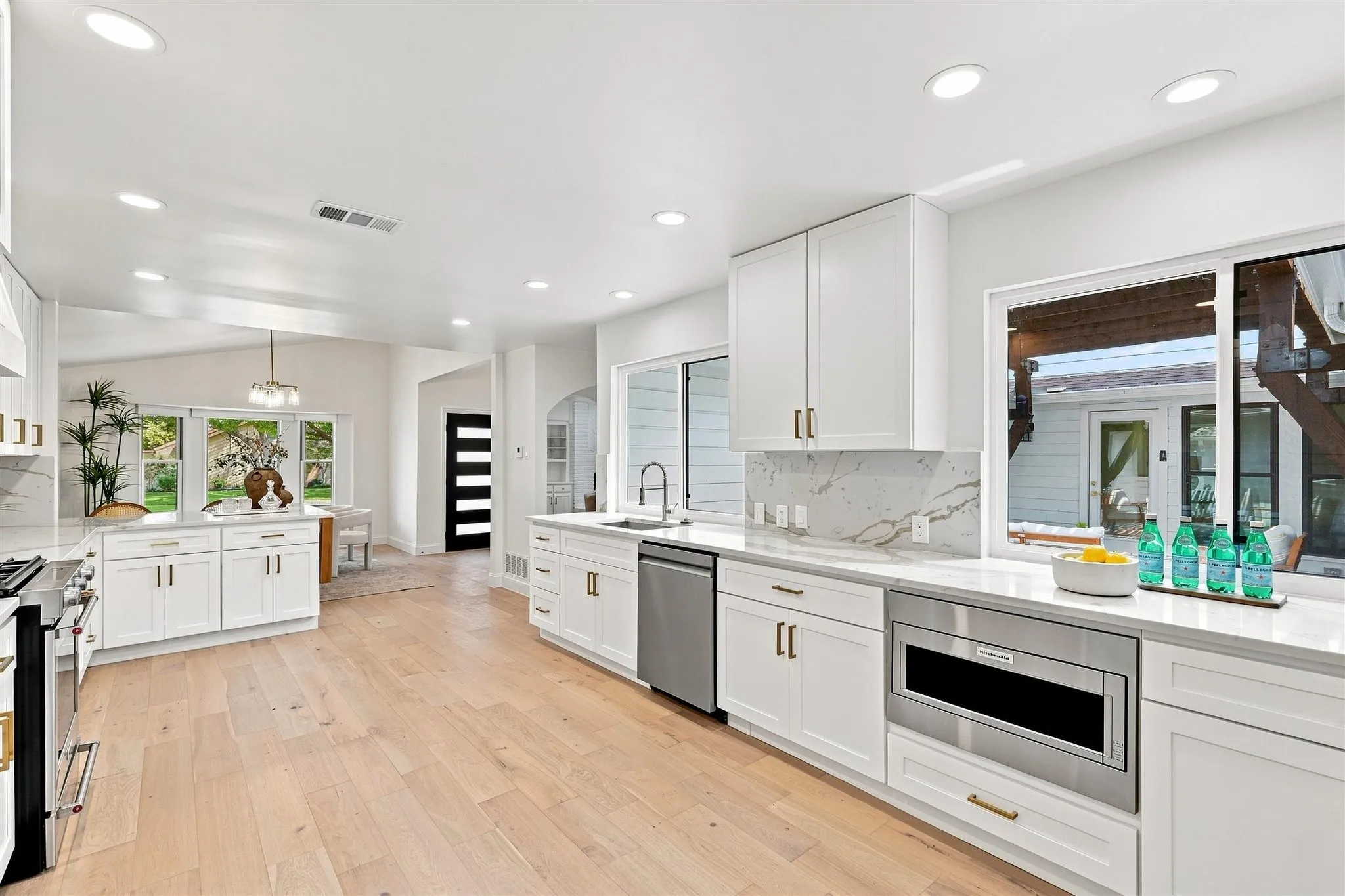 Gourmet kitchen with wood-finish flooring, white cabinetry, integrated stainless steel appliances, and quartz countertops with a matching backsplash