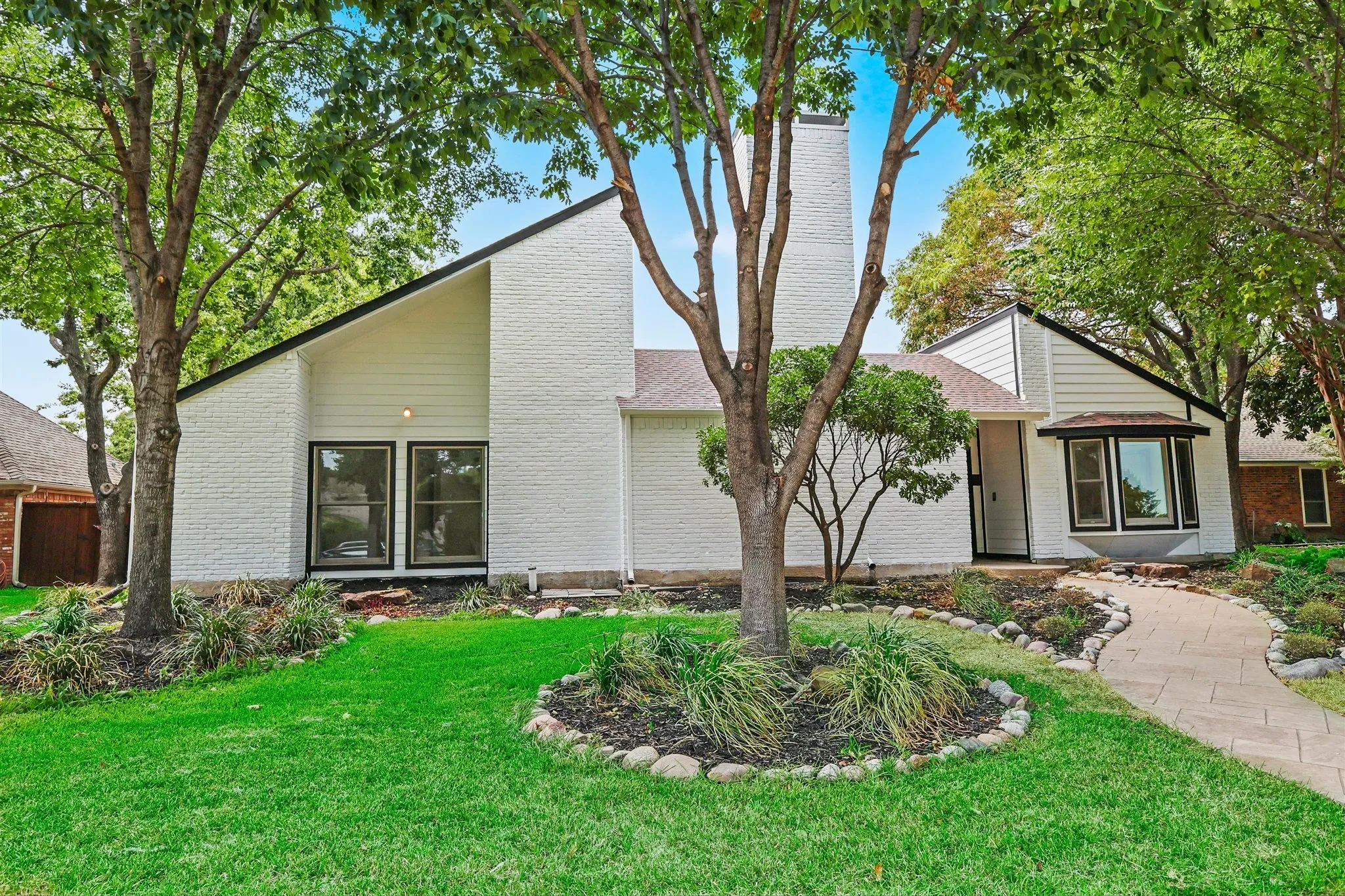 White brick exterior featuring a prominent chimney, angled roofline, and a bay window