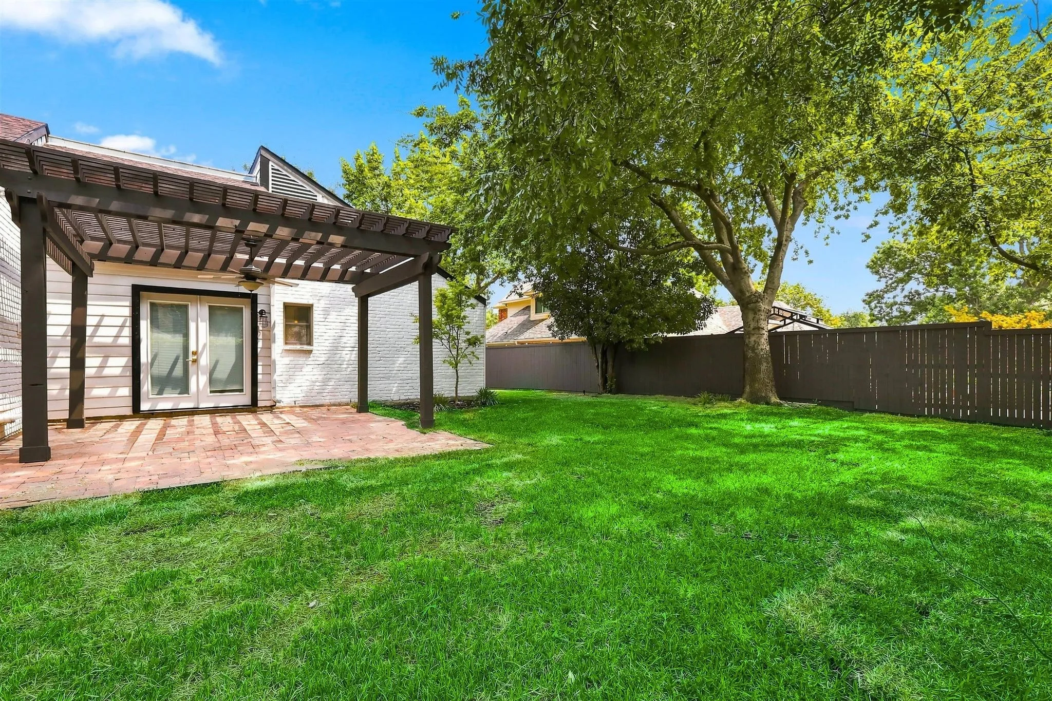 Expansive rear lawn, privacy fencing, mature trees, brick patio, and a wood pergola