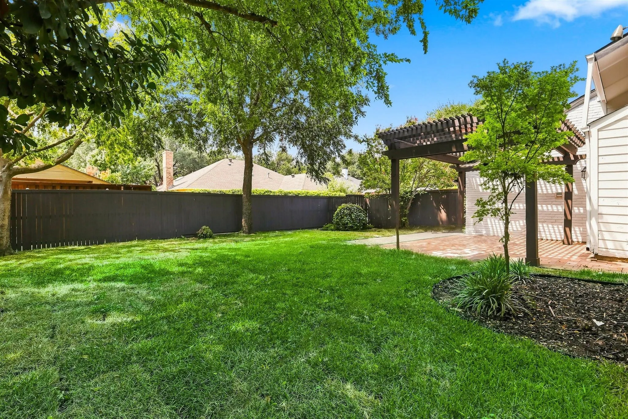 Expansive backyard featuring a manicured lawn, full privacy fencing, and a wooden pergola over a paved patio
