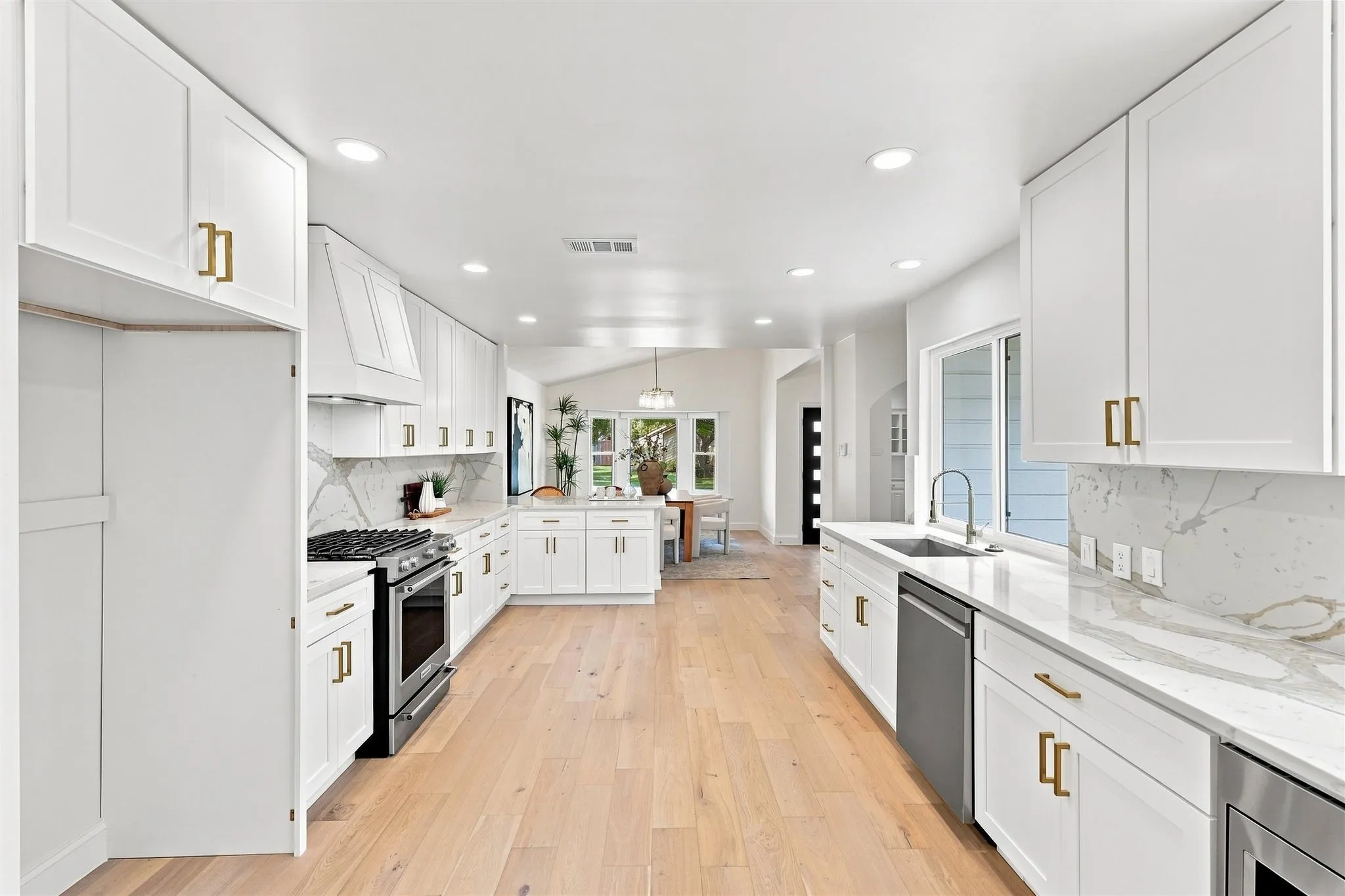 Bright kitchen featuring white shaker cabinetry, light wood-finish flooring, recessed lighting, and stainless steel appliances