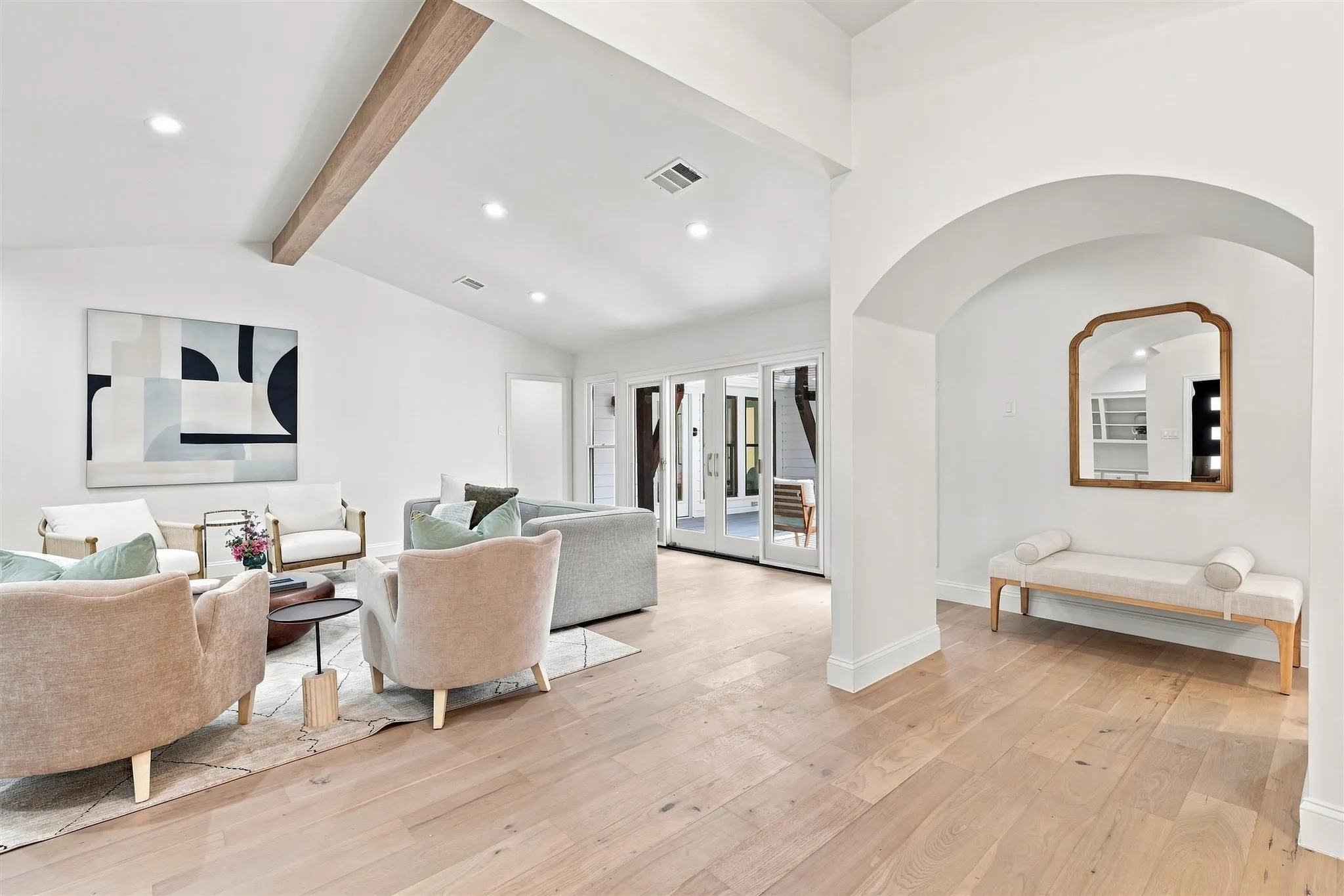 Vaulted ceiling with wood beam accent, light wood-finish flooring, recessed lighting, and arched doorway