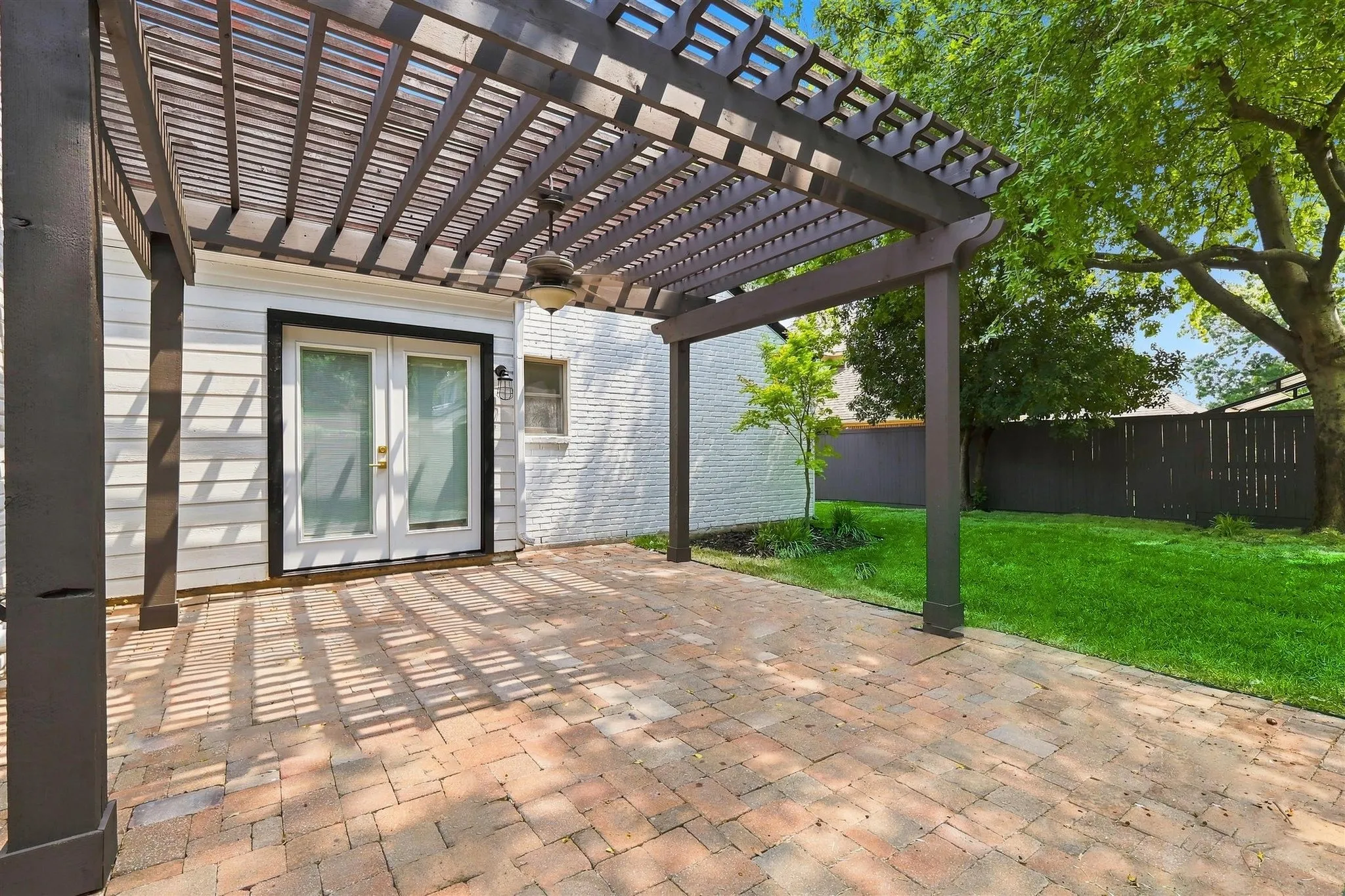 Paver patio with a dark wood pergola, ceiling fan, and access to the interior via double glass doors