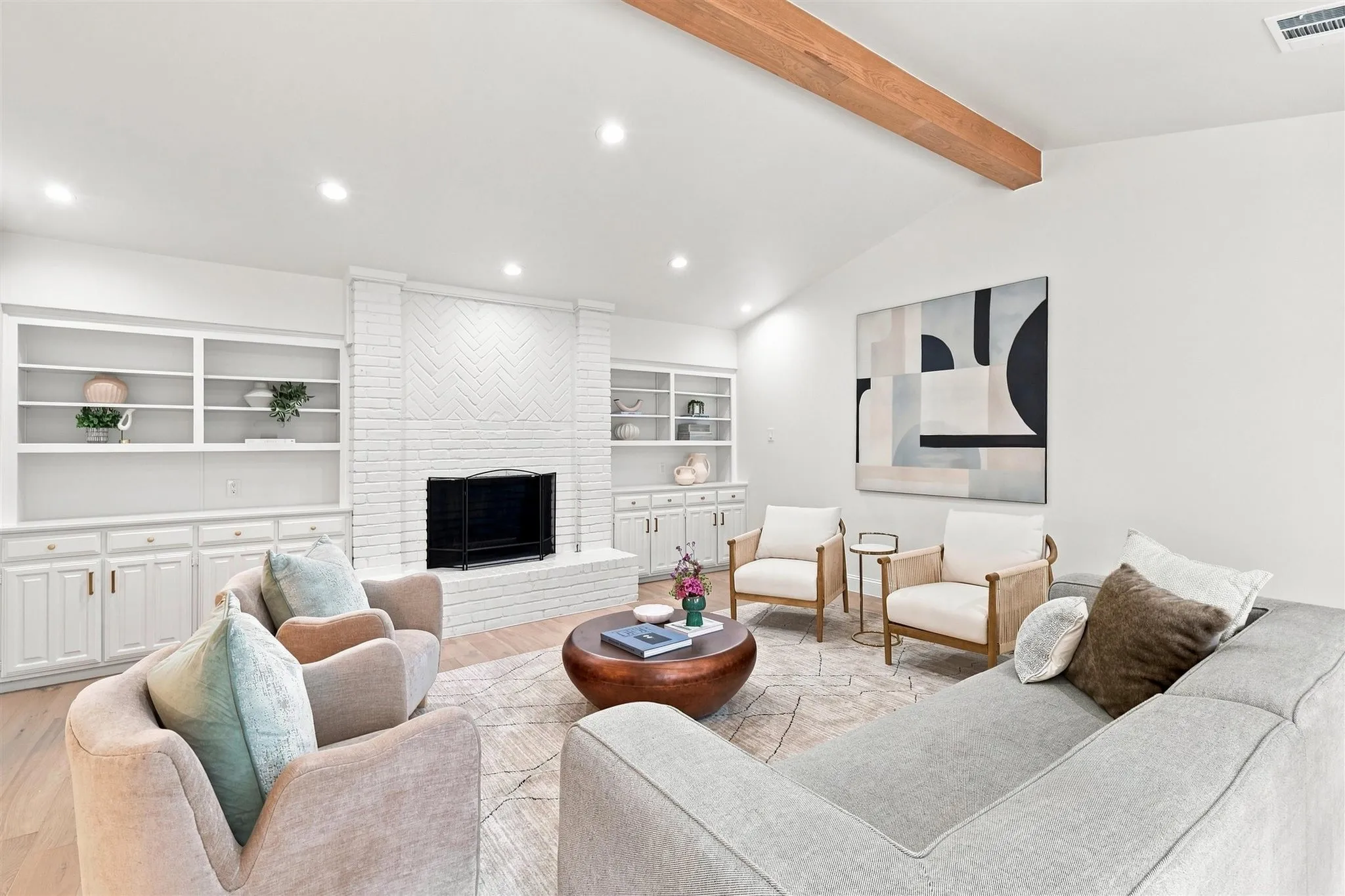 Vaulted ceiling with wood-finish beam, white painted brick fireplace, recessed lighting, and built-in cabinetry with shelving