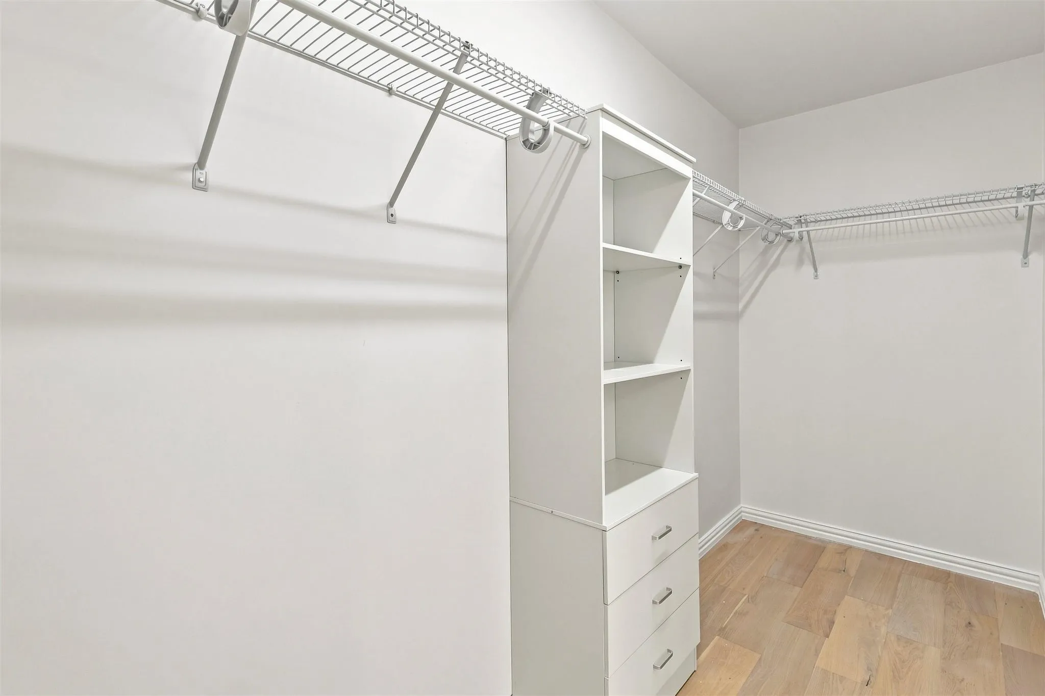 Walk-in closet with wire shelving, built-in drawer storage, and wood-finish flooring
