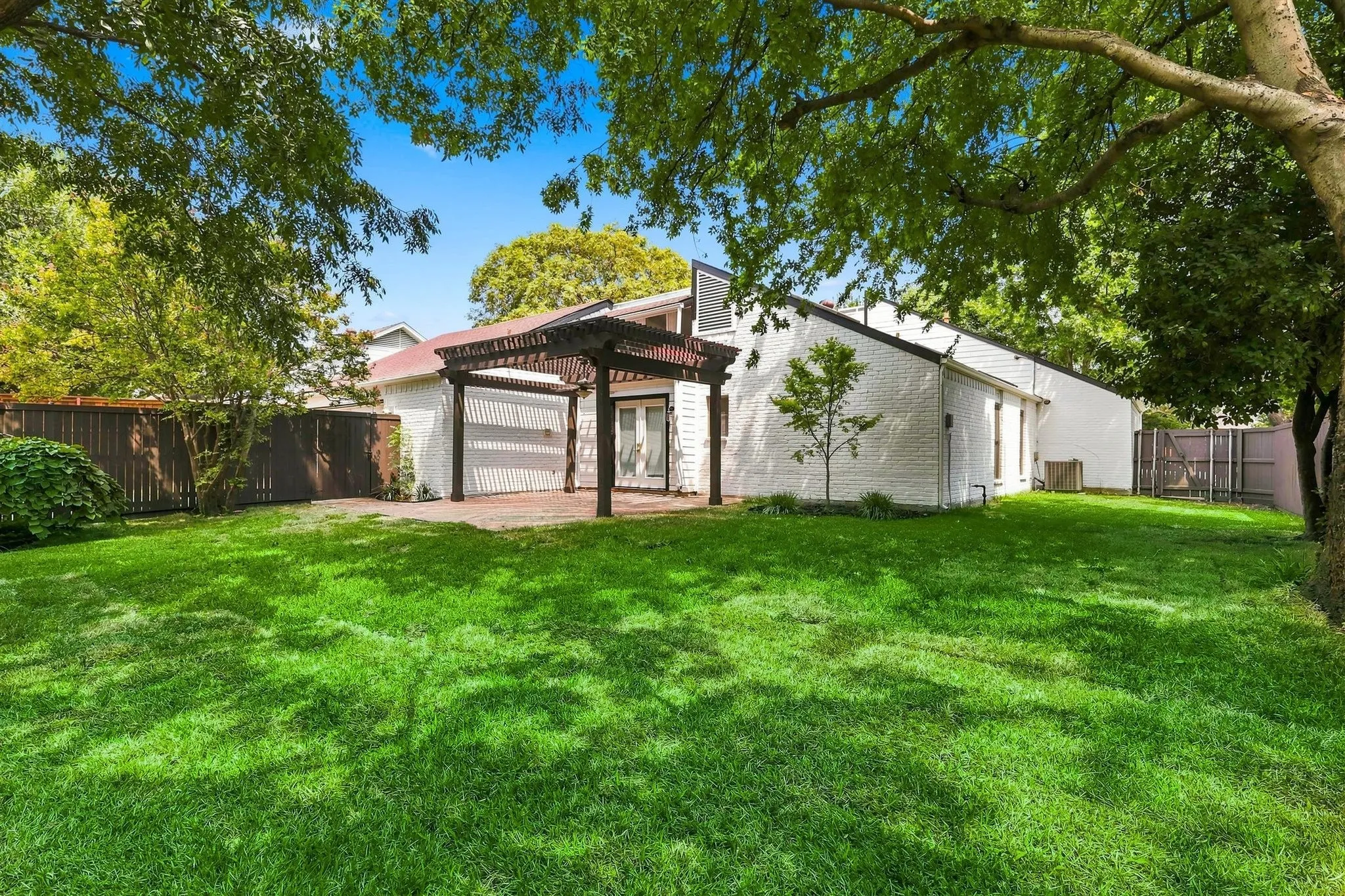 Expansive lawn with mature trees, brick patio, and a pergola