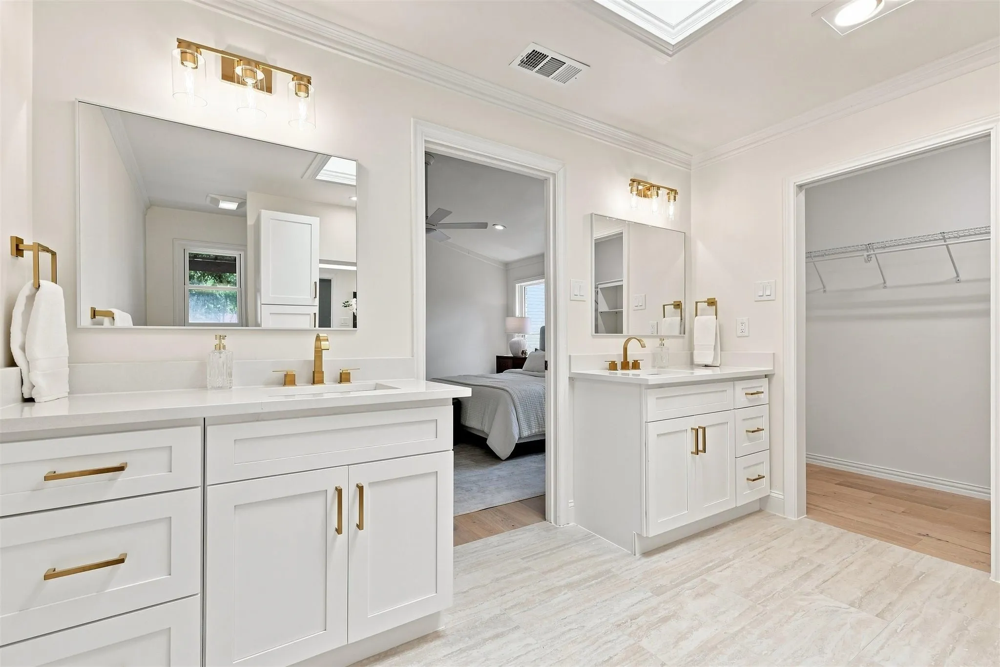 Dual vanity bathroom featuring light wood-finish flooring, white cabinetry, and gold-finish fixtures