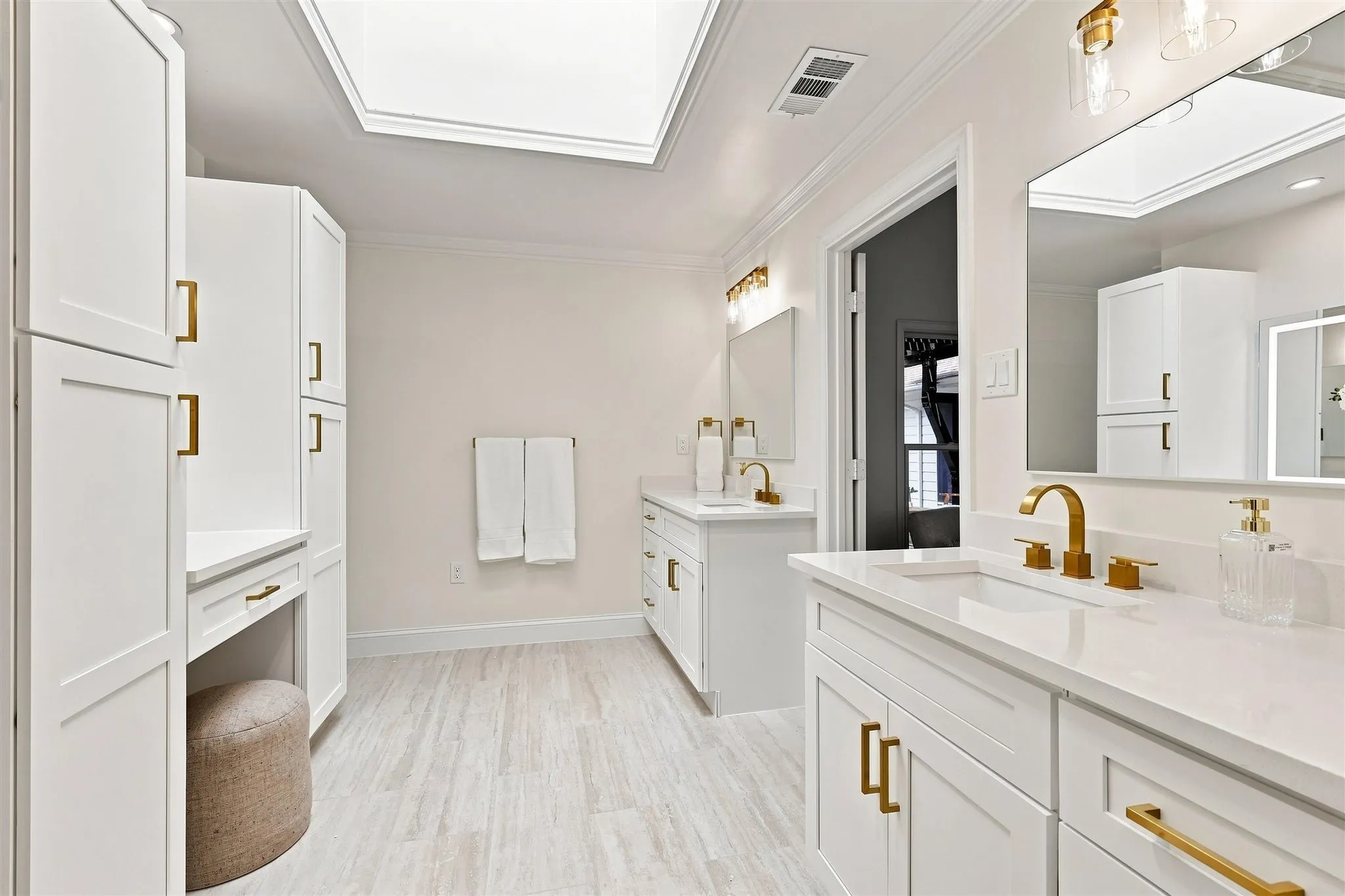Dual vanity with integrated sinks, gold-finish fixtures, white cabinetry with gold-finish hardware, and a skylight