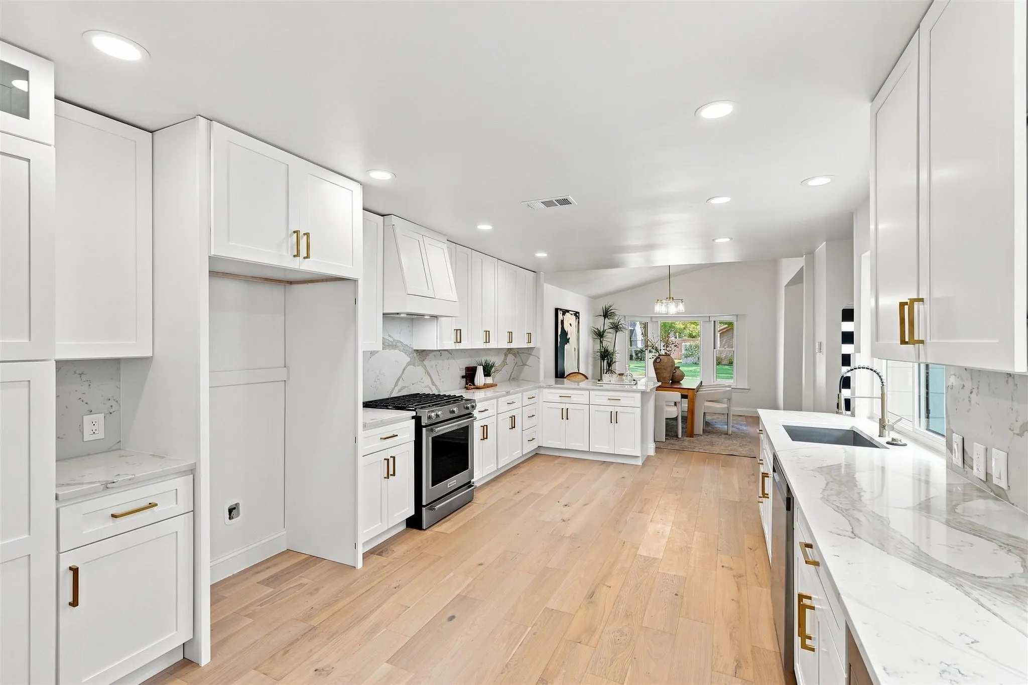 Spacious kitchen featuring white cabinetry, light wood-finish flooring, white countertops with integrated sink, stainless steel appliances, and recessed lighting
