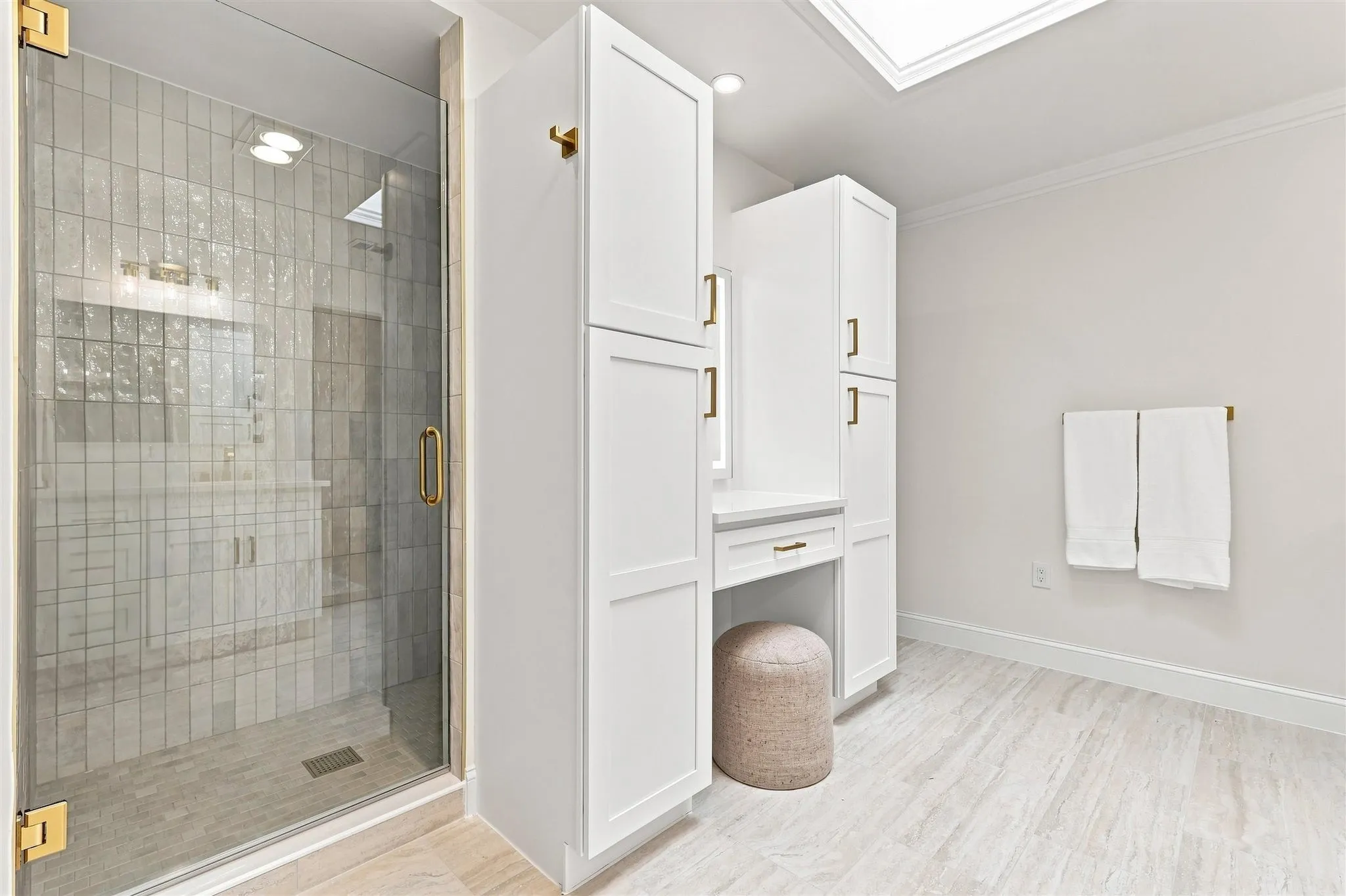 Glass-enclosed shower with gold-tone hardware, floor-to-ceiling tile, and a recessed light