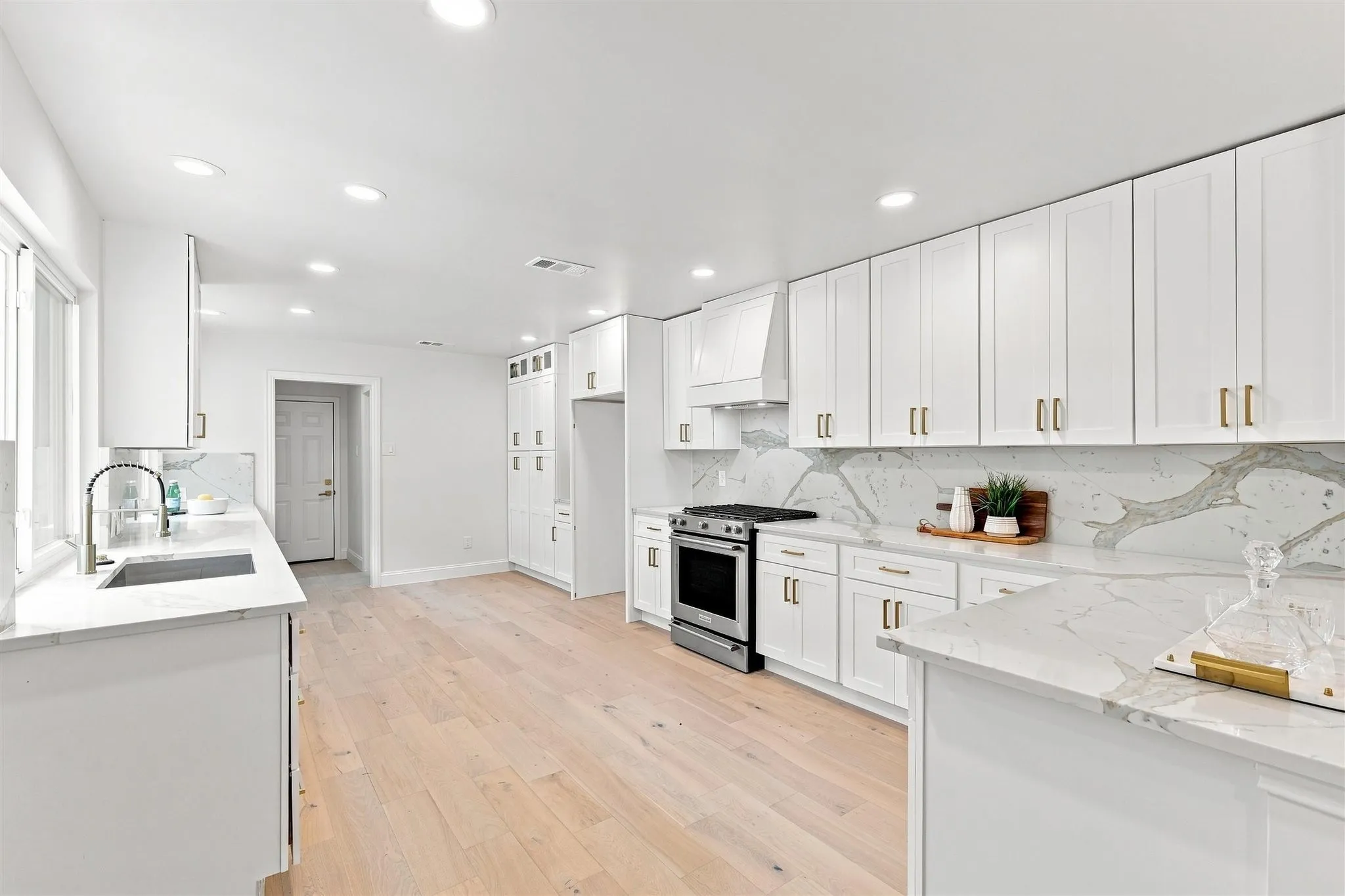 Kitchen featuring light wood-finish flooring, white shaker cabinetry with gold-tone hardware, and light-toned countertops with a matching backsplash